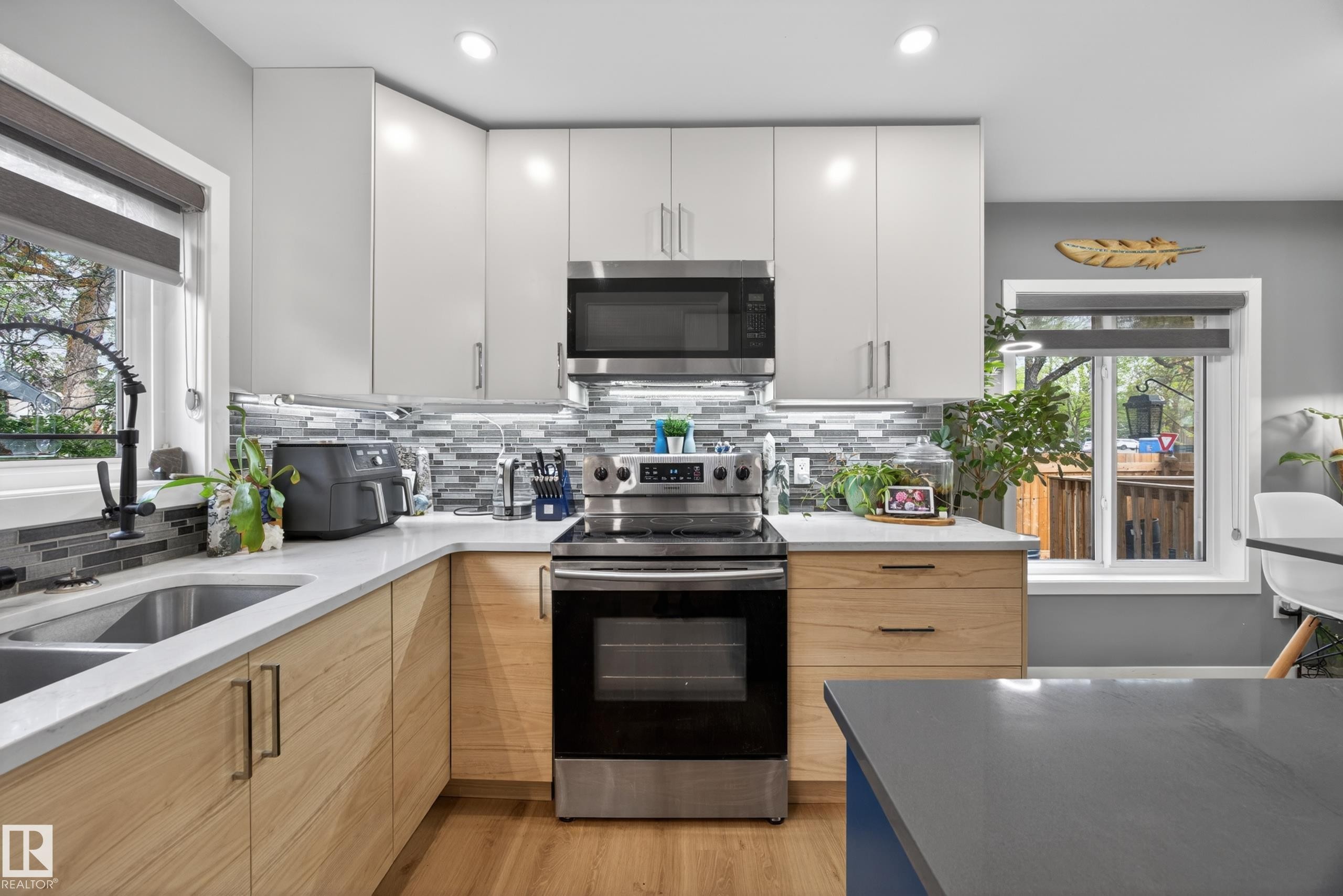 Modern kitchen featuring light wood-finish lower cabinetry, white upper cabinetry, and stainless steel appliances - 12604 116 Avenue, Edmonton, AB