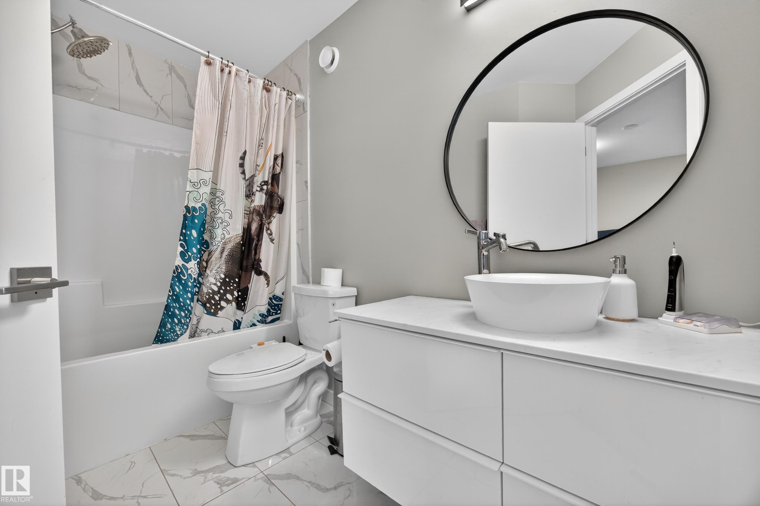Bathroom featuring a white vanity with vessel sink, oval mirror, and a shower-tub combination with tile surround - 12604 116 Avenue, Edmonton, AB