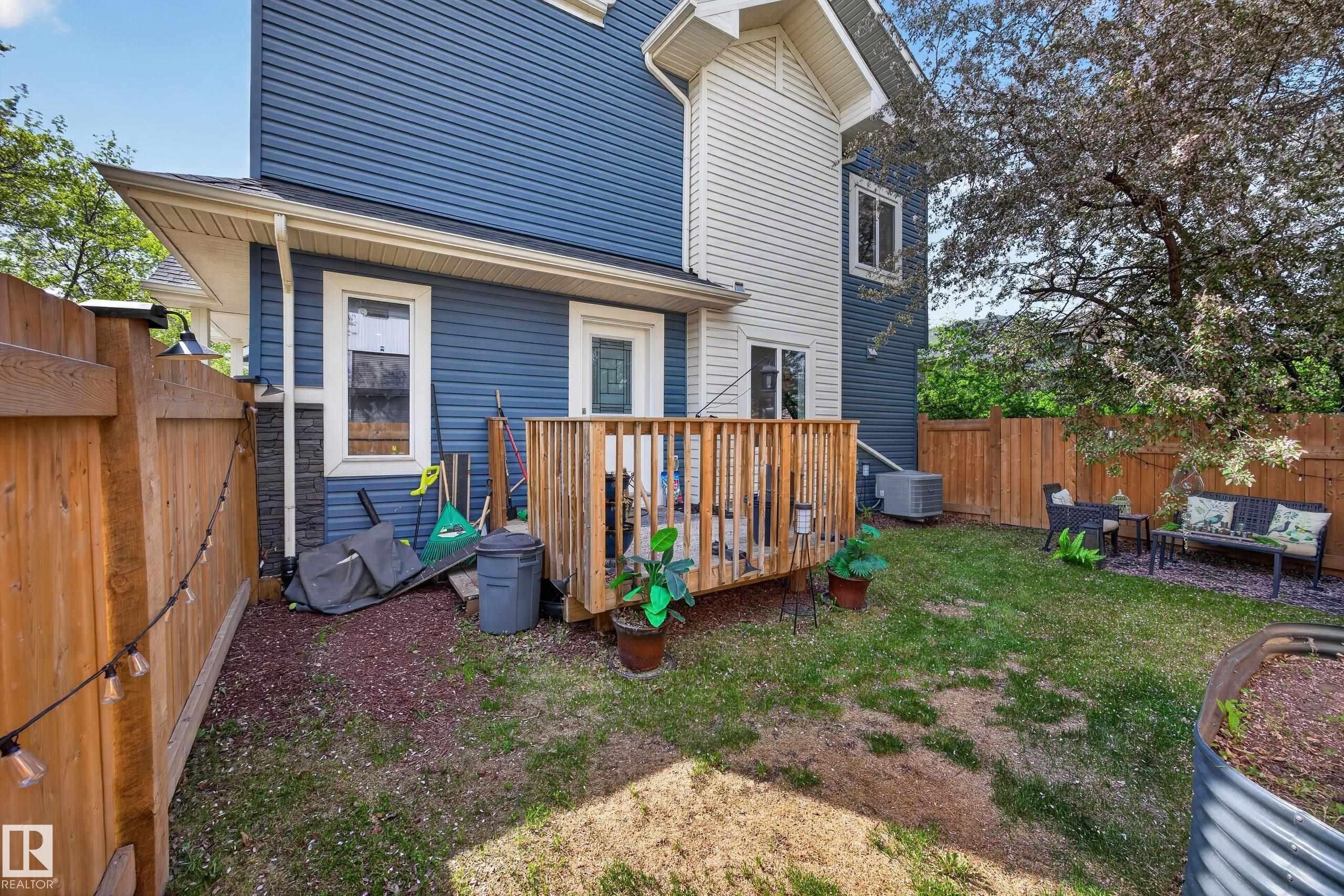 Fenced backyard featuring a wooden deck, established trees, and a raised garden bed - 12604 116 Avenue, Edmonton, AB