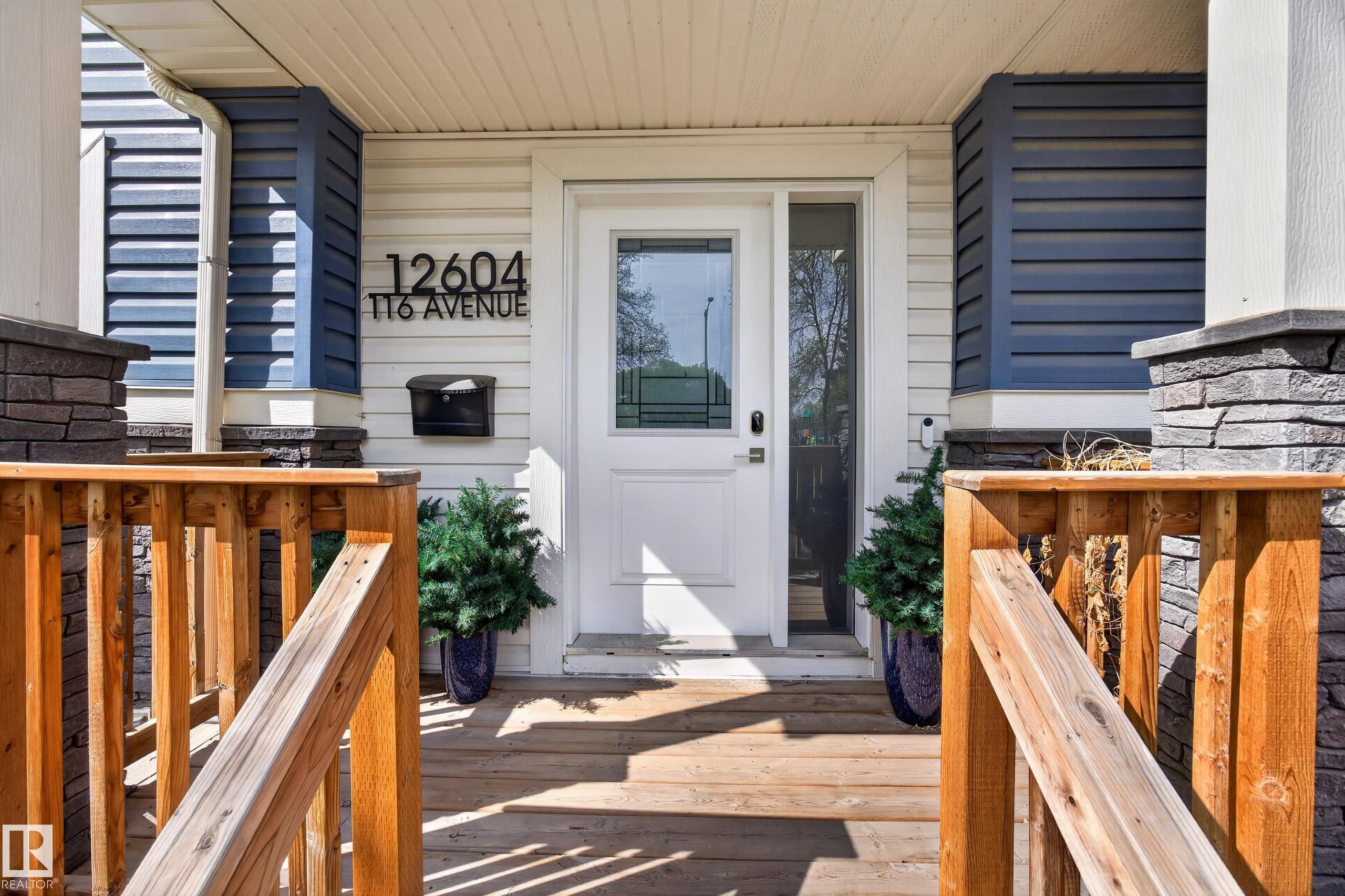 Inviting front entrance featuring a white panel door with sidelight, light-colored siding, and contrasting blue horizontal accents - 12604 116 Avenue, Edmonton, AB