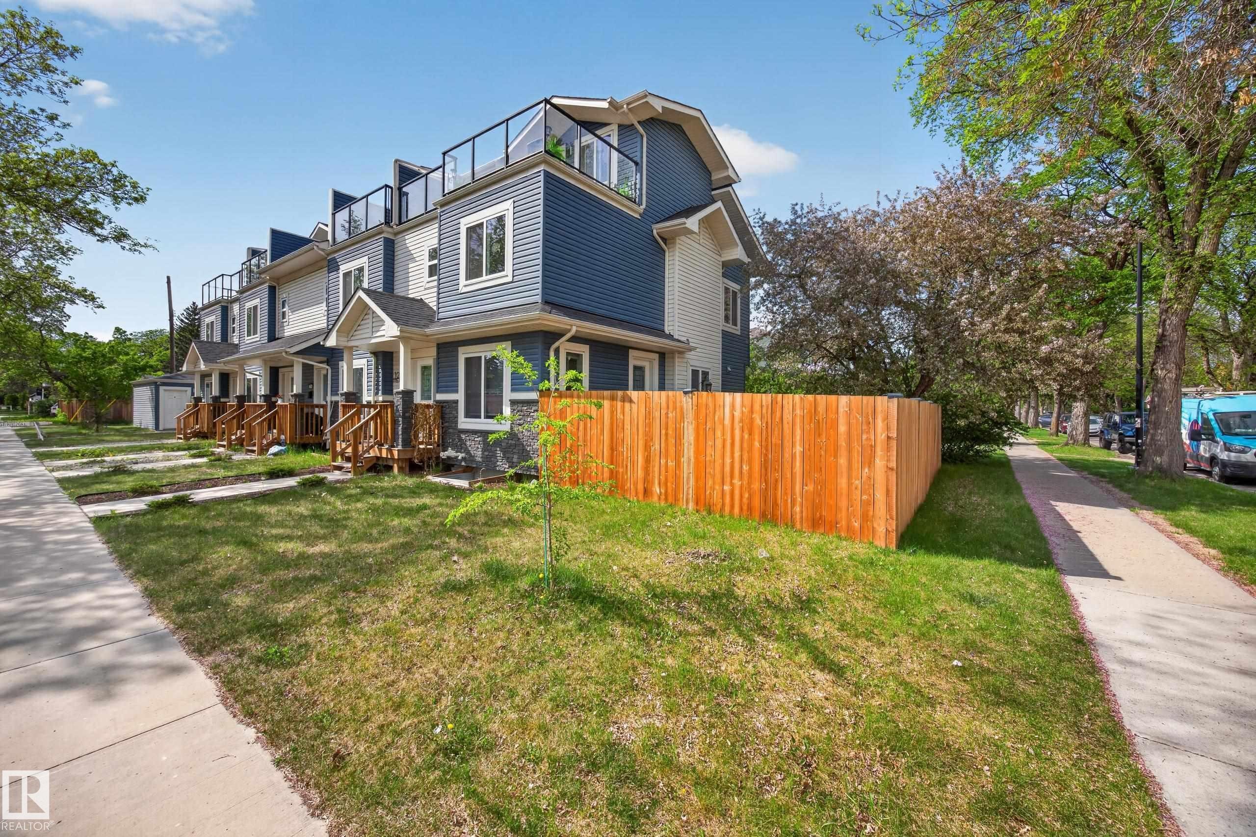 Modern townhome exterior featuring blue and white siding, stone veneer accents, and a third-story rooftop deck with glass railings - 12604 116 Avenue, Edmonton, AB