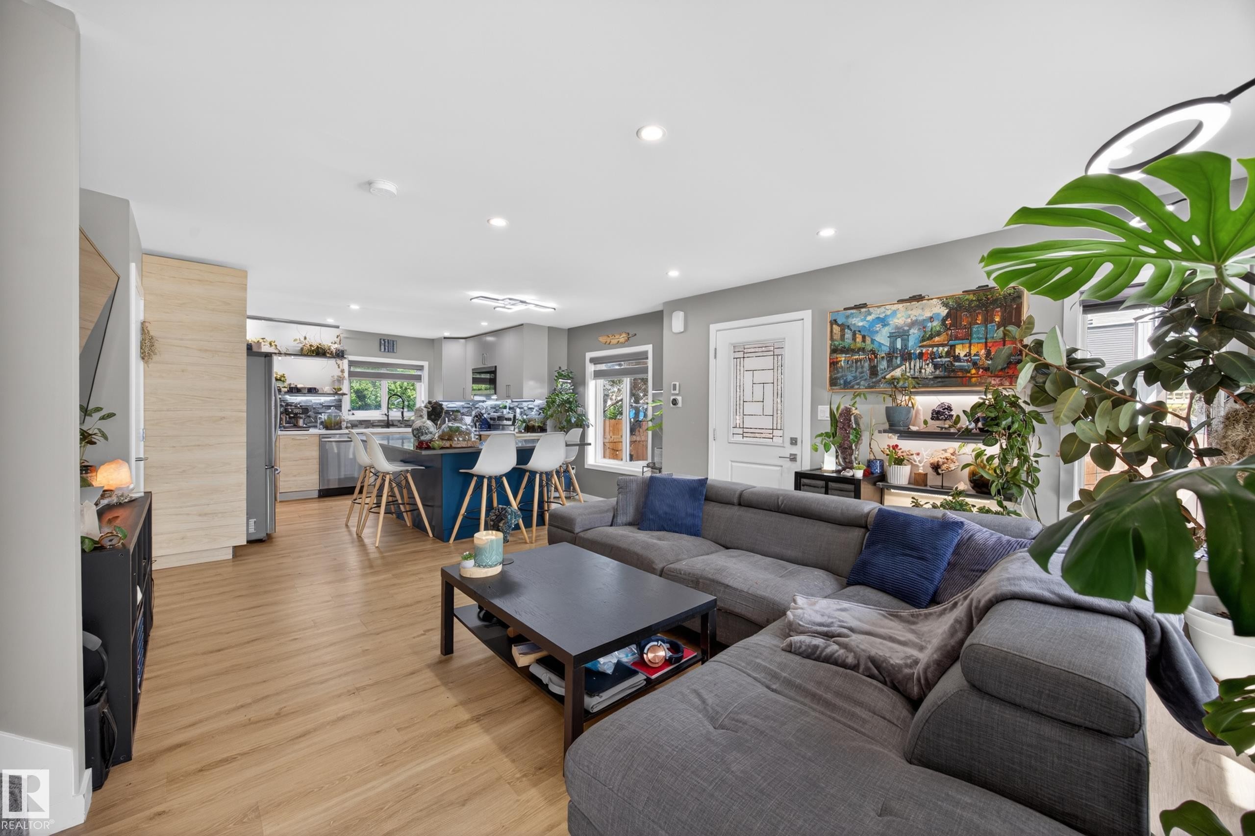 Open-concept living space featuring wood-finish flooring, recessed lighting, and a kitchen with an island, light-toned cabinetry, and stainless steel appliances - 12604 116 Avenue, Edmonton, AB