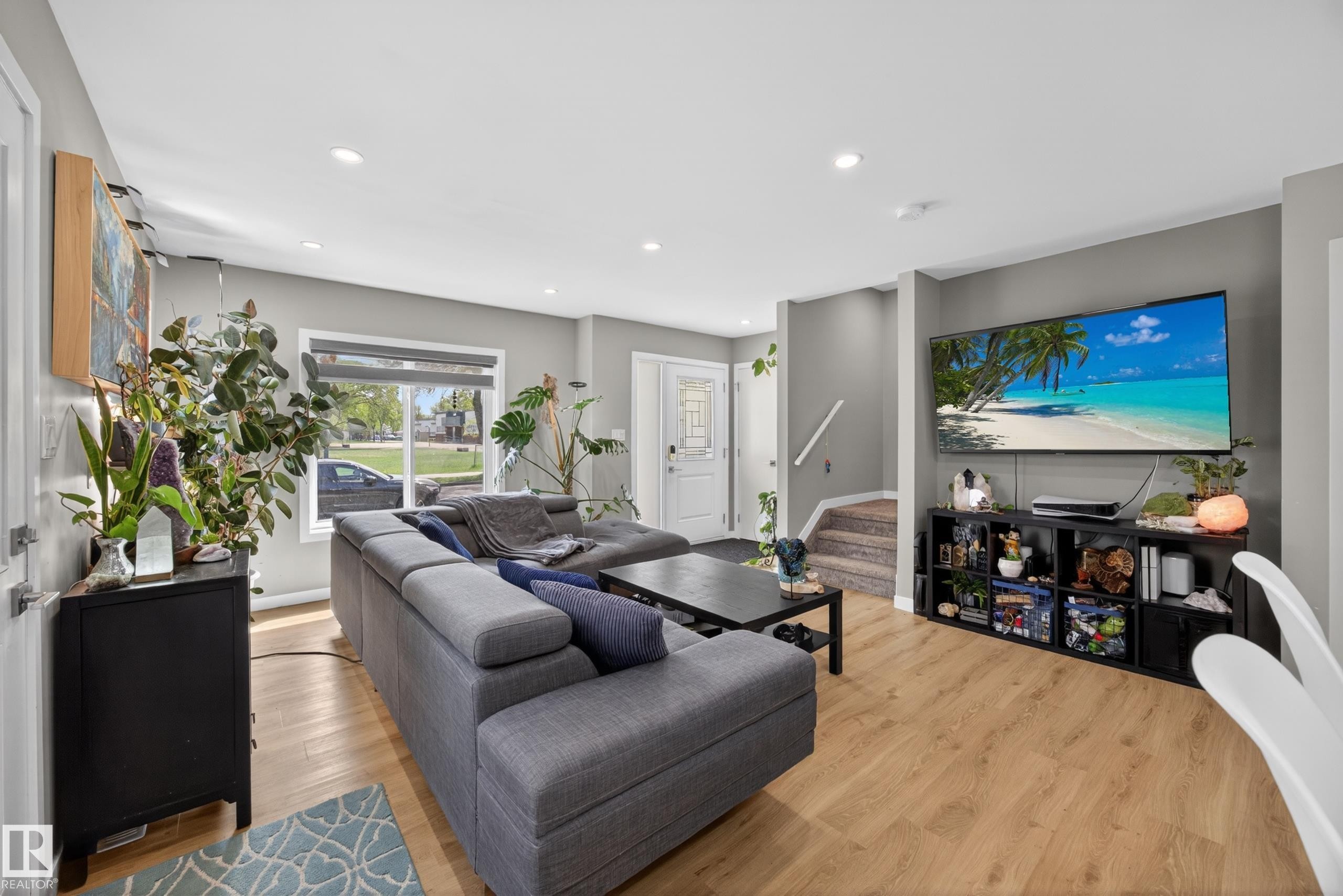 Open-concept living space featuring wood-finish flooring, recessed lighting, and a white front entry door with a decorative glass insert - 12604 116 Avenue, Edmonton, AB