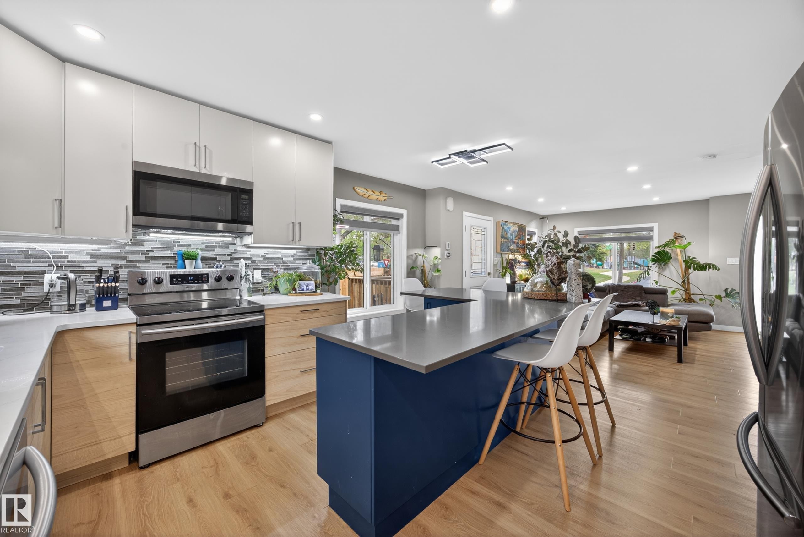 Open-concept kitchen featuring a two-tone cabinetry design, stainless steel appliances, and a blue island with a contrasting countertop - 12604 116 Avenue, Edmonton, AB