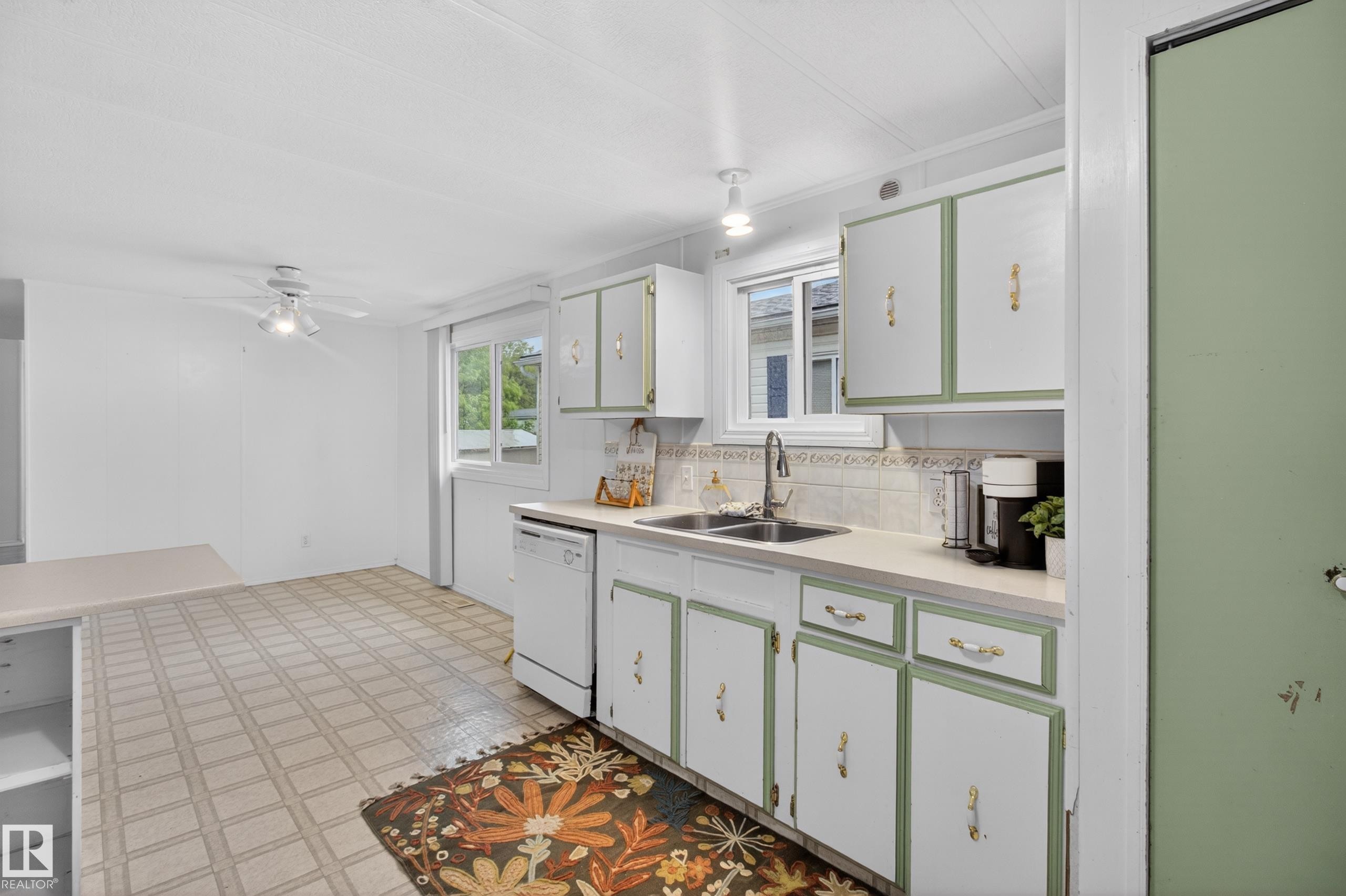Kitchen featuring white cabinetry with green trim, a dual basin sink with a gooseneck faucet, light-toned countertops, and a patterned tile backsplash - 21 Willowdale Drive, Edmonton, AB - Indoor Photo Showing Kitchen With Double Sink