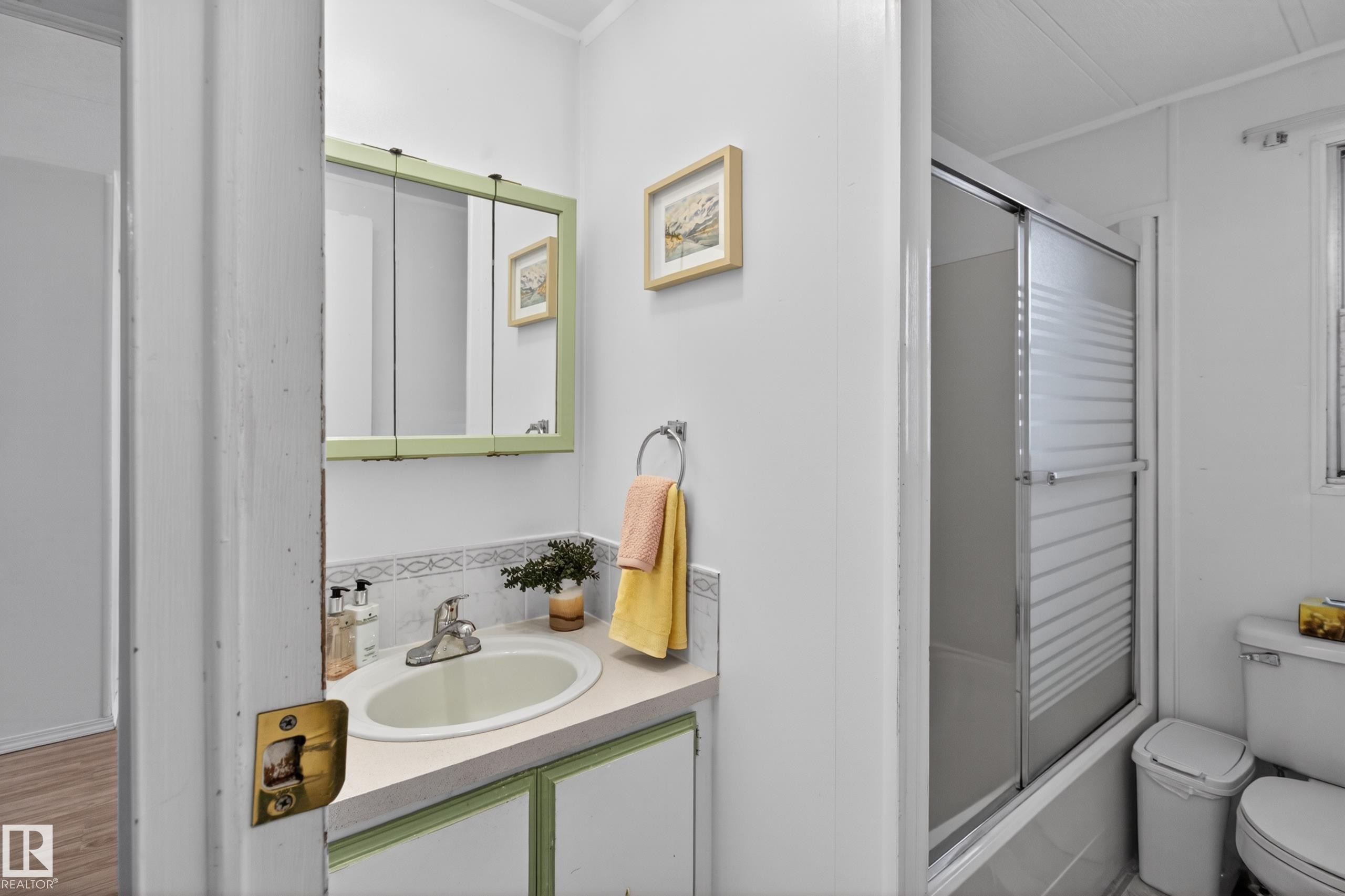 Bathroom featuring a vanity with a white countertop and integrated sink, a medicine cabinet with a light green frame, a shower-over-tub with a sliding frosted glass door, and tiled walls - 21 Willowdale Drive, Edmonton, AB - Indoor Photo Showing Bathroom