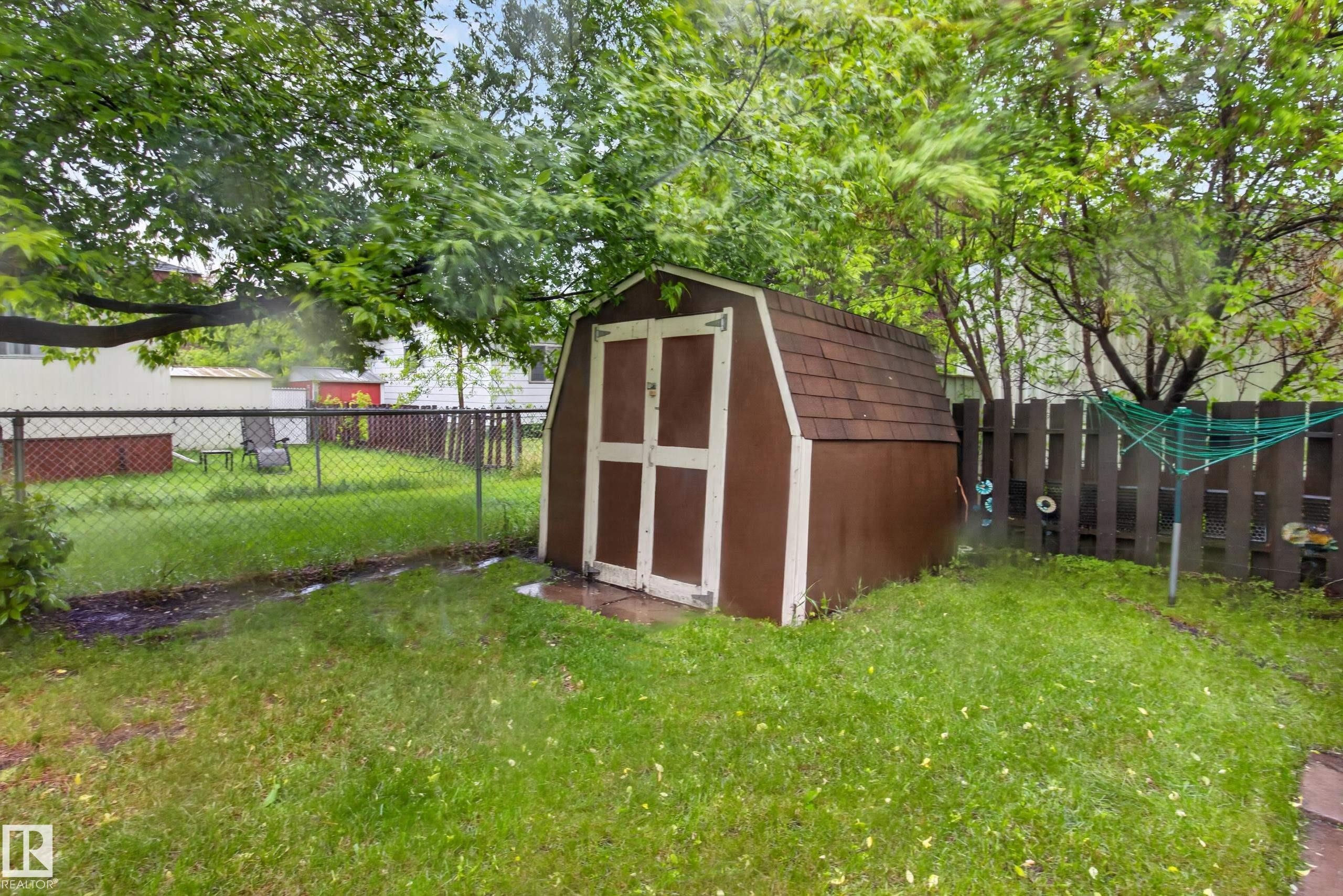 Backyard featuring a brown shed with a gambrel roof and double white doors, surrounded by green lawn and mature trees - 21 Willowdale Drive, Edmonton, AB - Outdoor