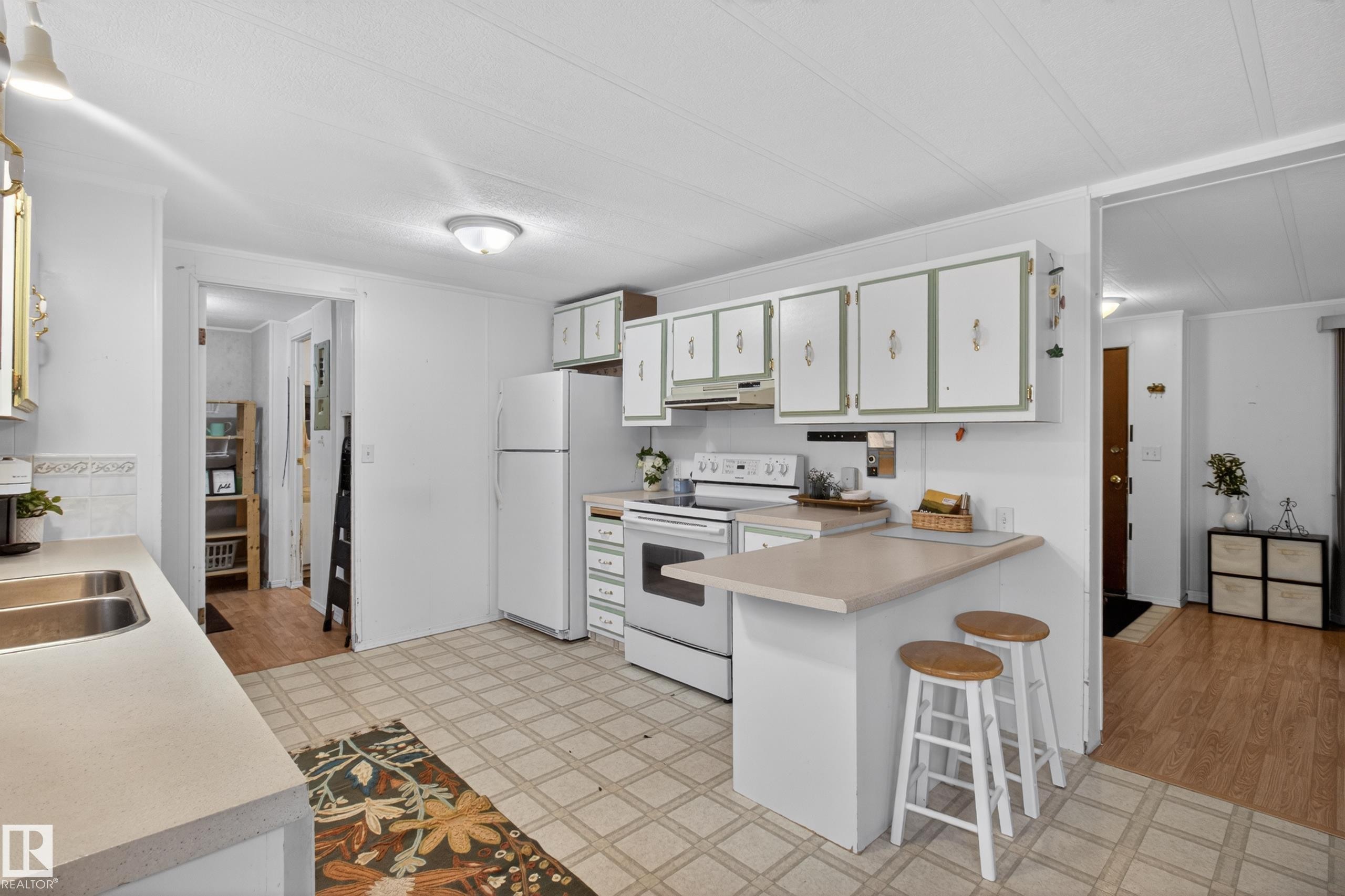 Kitchen featuring a double basin stainless steel sink, white cabinetry with decorative hardware, a built-in electric range, and a breakfast bar - 21 Willowdale Drive, Edmonton, AB - Indoor Photo Showing Kitchen With Double Sink
