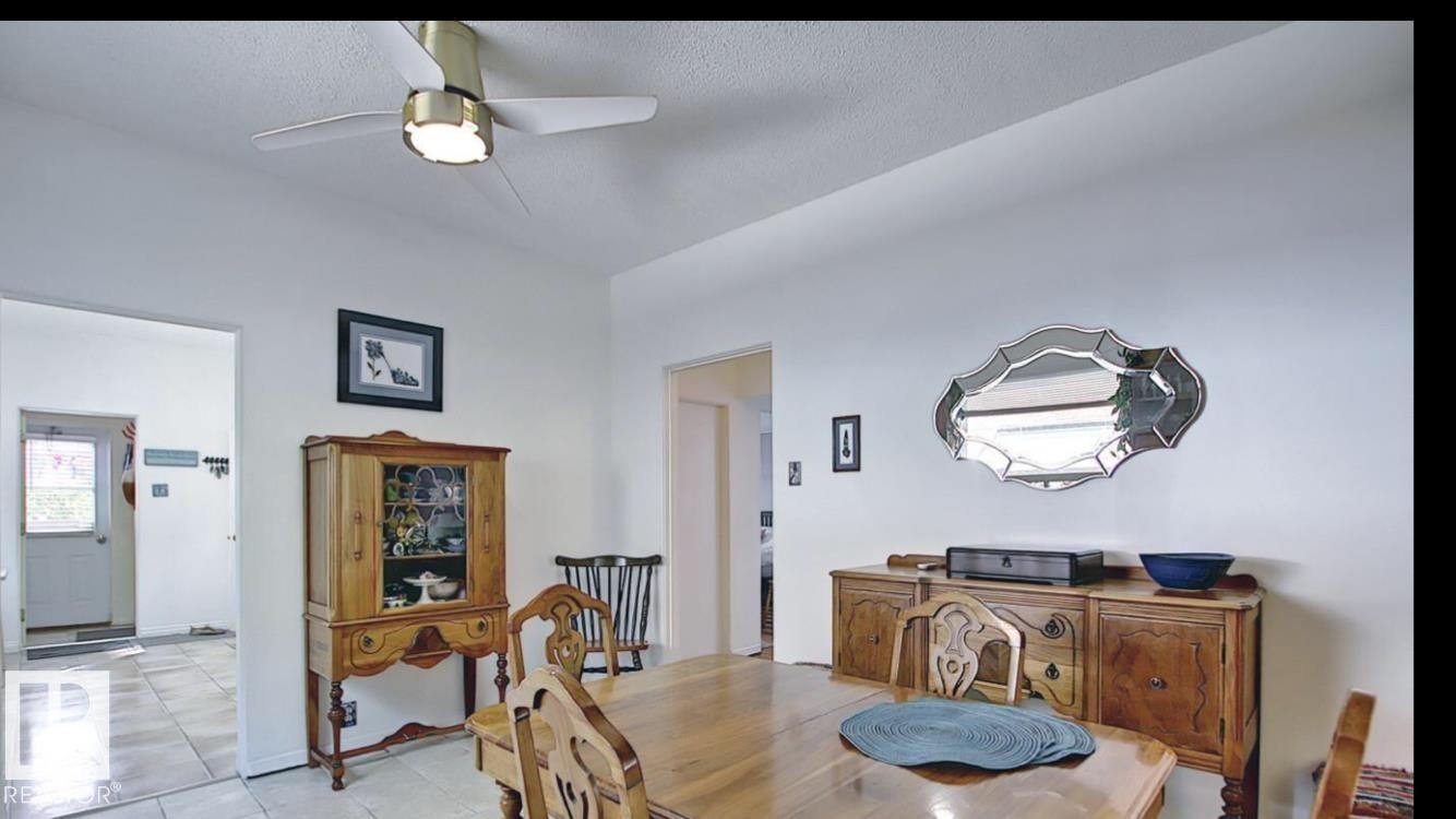Dining area featuring a ceiling fan with integrated lighting, a decorative wall mirror, and a tiled floor visible through the doorway - 10017 113 Street, Edmonton, AB