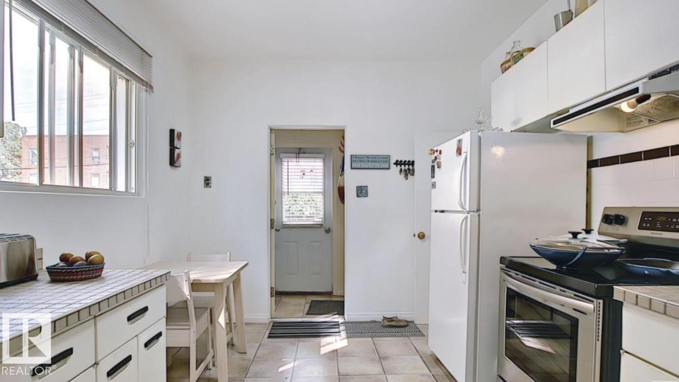 Kitchen featuring white cabinetry, tile countertops, and a white refrigerator - 10017 113 Street, Edmonton, AB