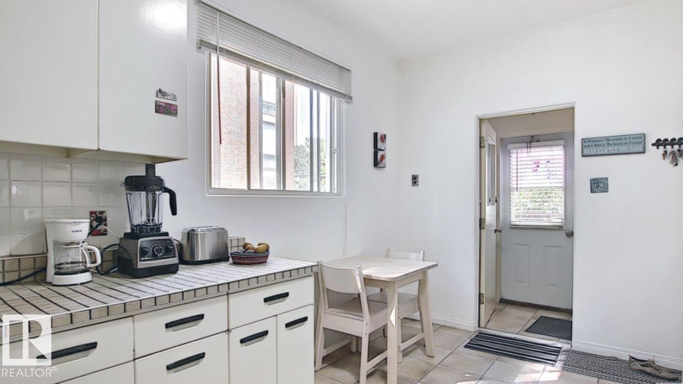 Kitchen with white cabinetry, tile countertops, and a full-light exterior door - 10017 113 Street, Edmonton, AB