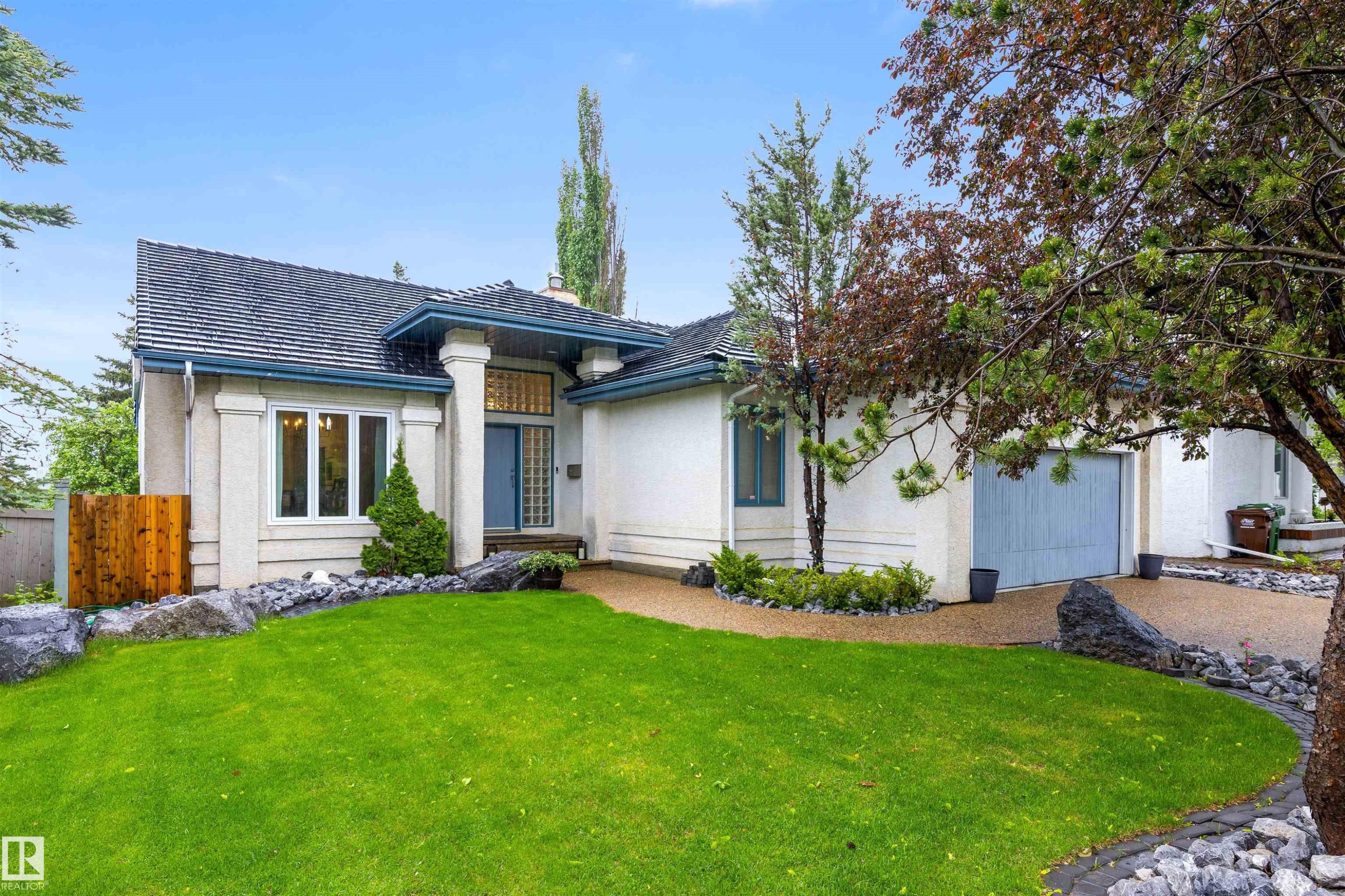 Stucco exterior with a dark shingle roof, two prominent front pillars, and a light blue front door - 10 Everest Crescent, St. Albert, AB