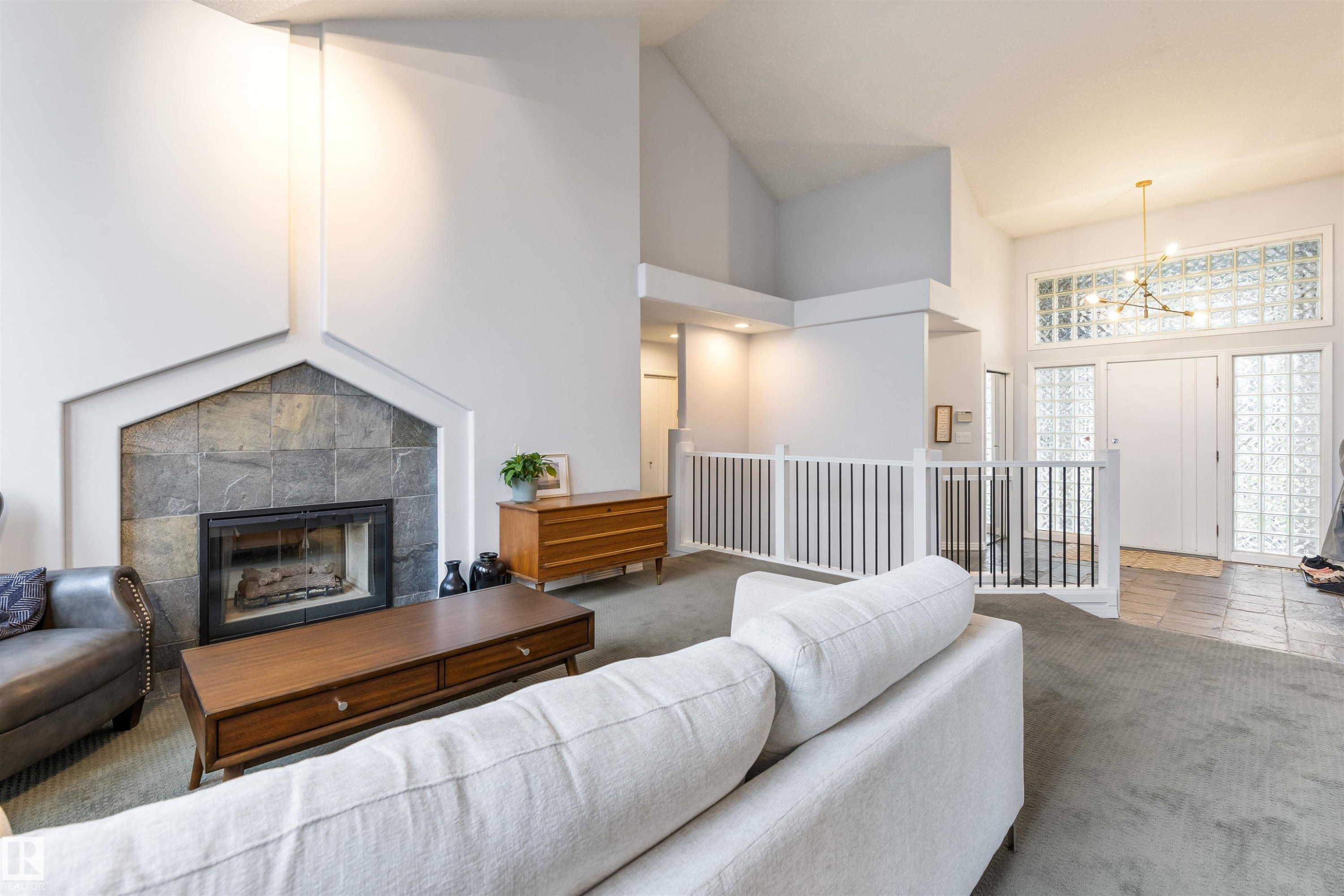 Living area featuring a stone-faced fireplace with a hearth, vaulted ceilings, and a decorative railing overlooking the entry - 10 Everest Crescent, St. Albert, AB