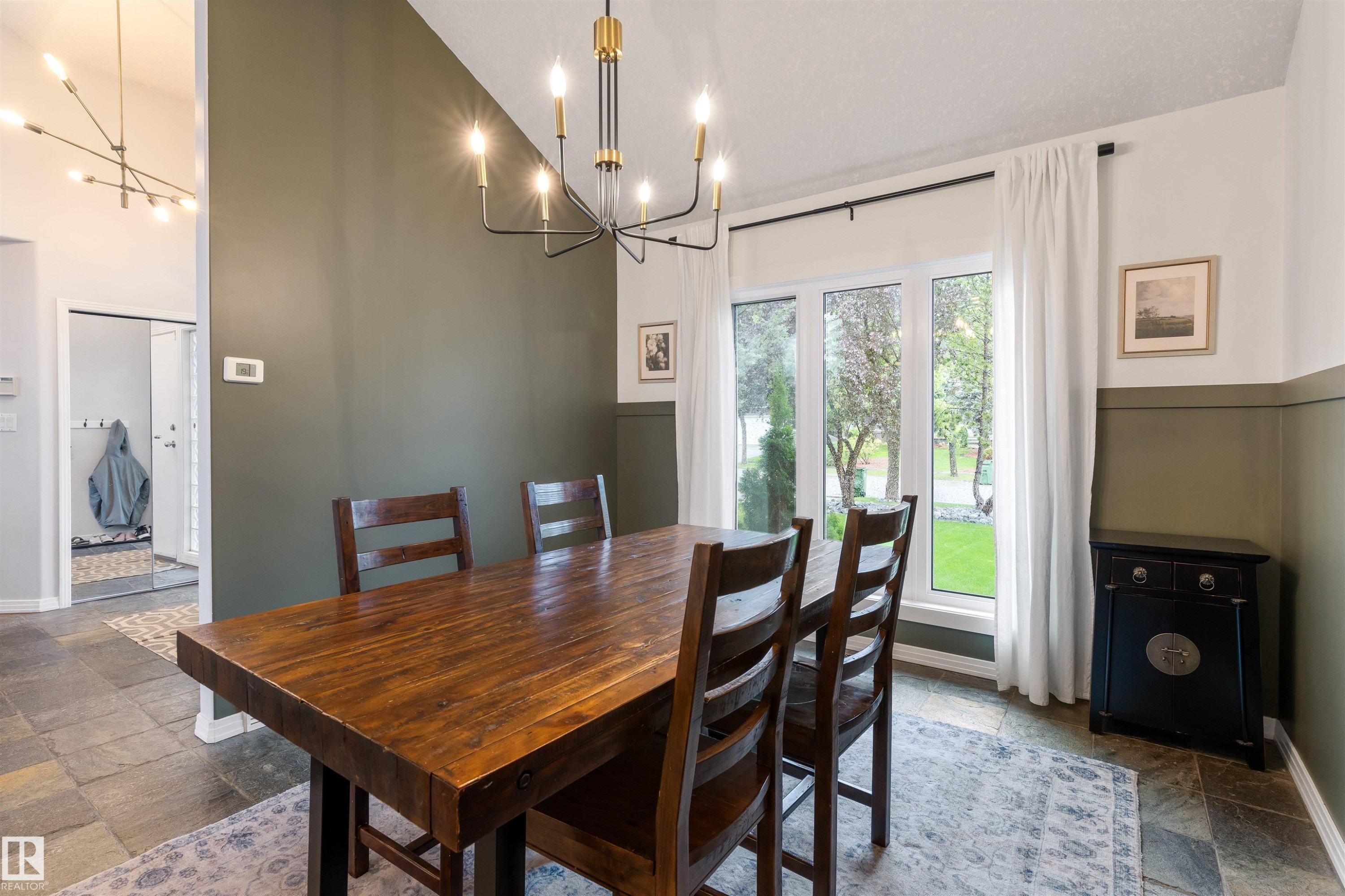 Dining space featuring slate tile flooring, a large window, a modern chandelier with gold accents, and a distinctive two-tone wall treatment - 10 Everest Crescent, St. Albert, AB