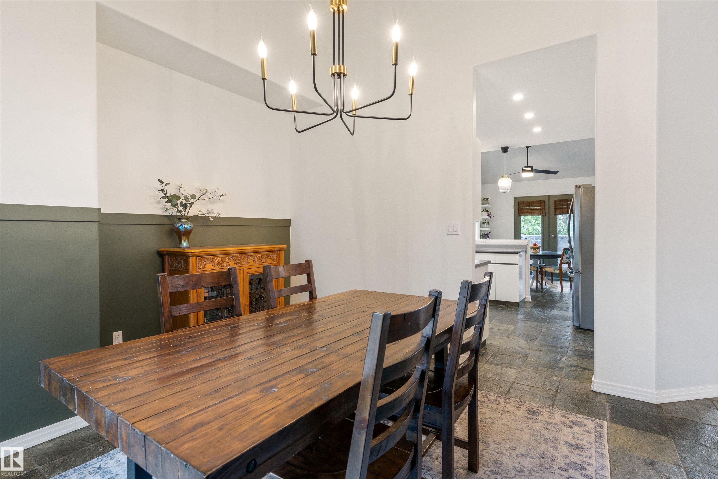 Spacious dining area featuring stone tile flooring, a contemporary chandelier, two-tone wall treatment, and an open doorway - 10 Everest Crescent, St. Albert, AB