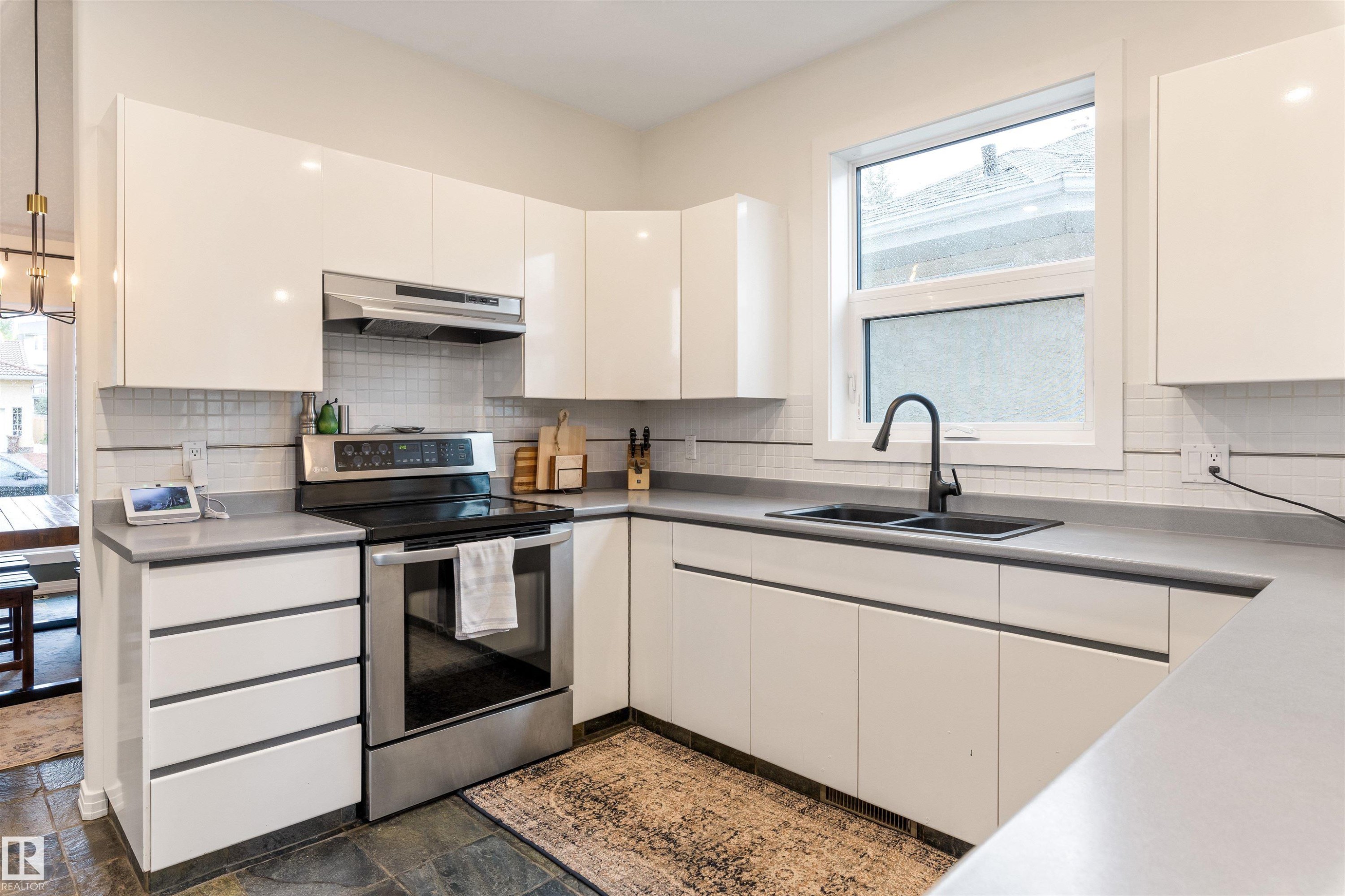 Contemporary kitchen featuring white high-gloss cabinetry, grey countertops, stainless steel appliances, a black undermount sink with a matte black faucet, and slate tile flooring - 10 Everest Crescent, St. Albert, AB