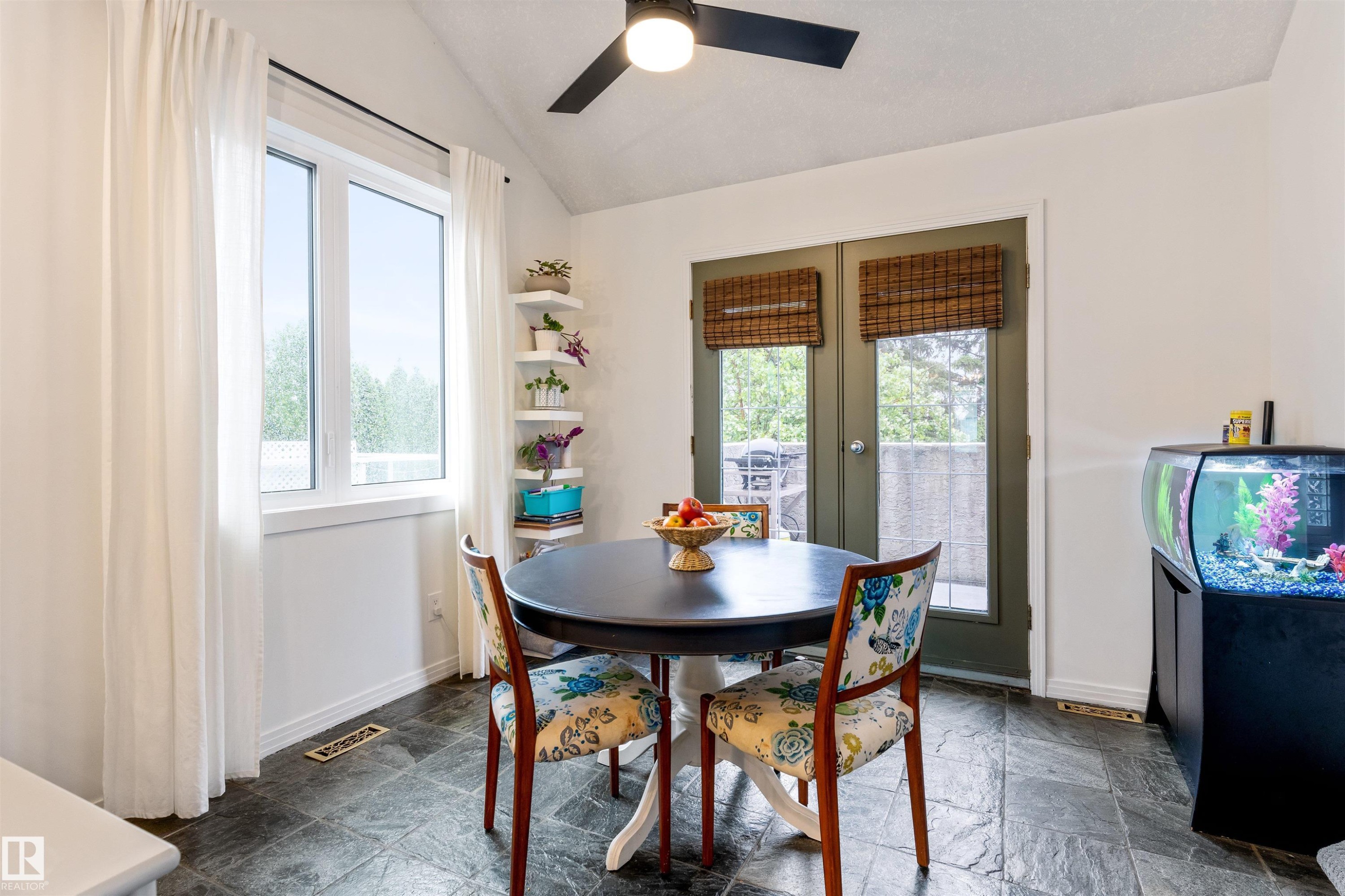 Dining area featuring a vaulted ceiling with a ceiling fan, a large casement window with white trim, and dark-framed double doors leading to an outdoor space - 10 Everest Crescent, St. Albert, AB