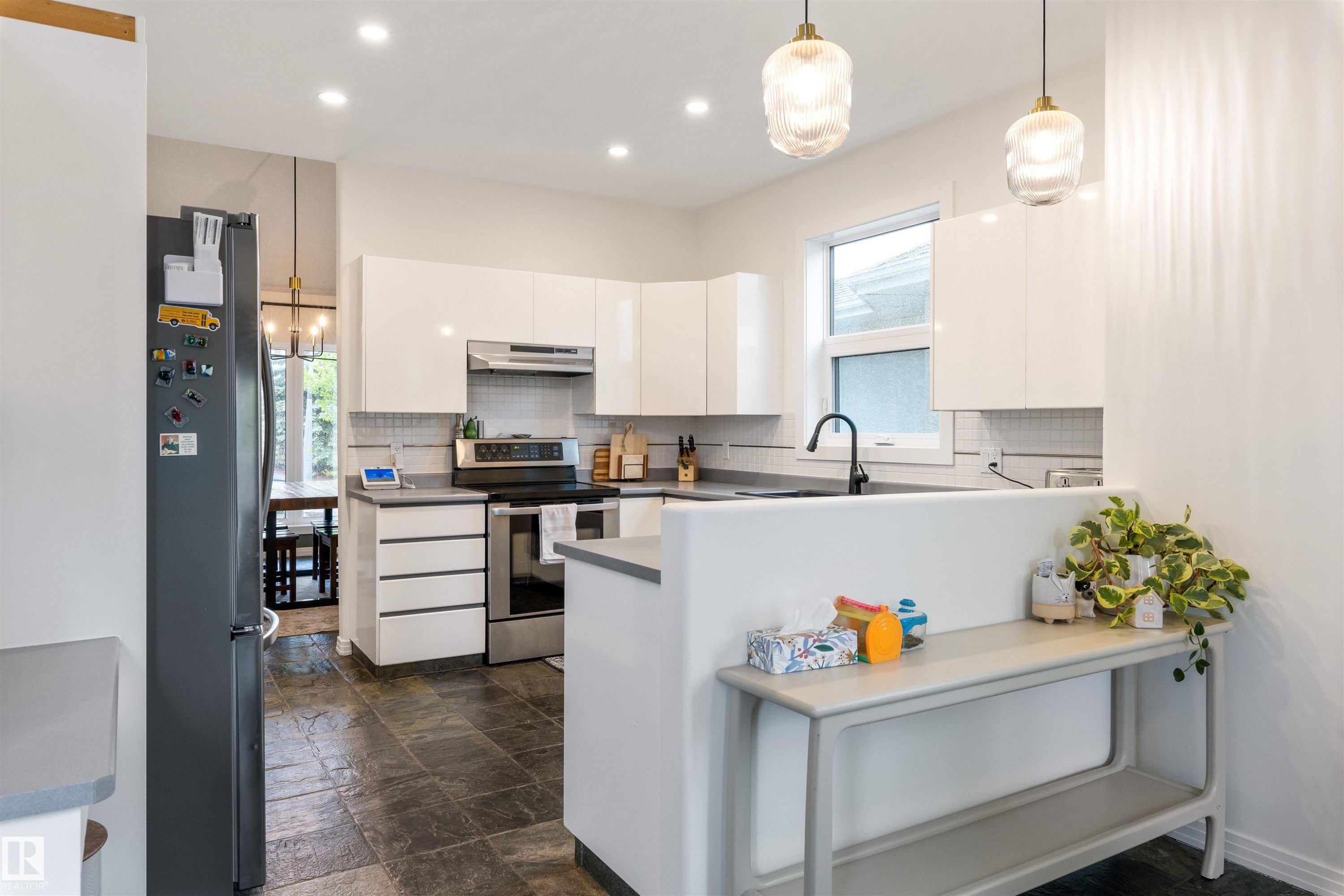 Modern kitchen featuring white flat-panel cabinetry, stainless steel appliances, a white subway tile backsplash, and dark stone floor tiles - 10 Everest Crescent, St. Albert, AB
