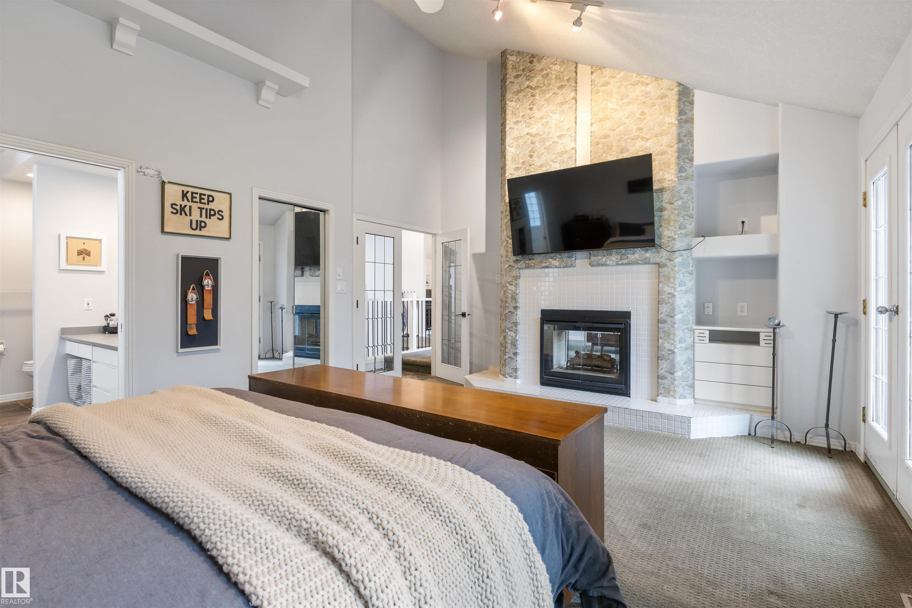 Vaulted ceiling room featuring a stone-clad fireplace with white tile surround, built-in shelving, two sets of French doors, and a separate entry to a vanity area with a built-in sink - 10 Everest Crescent, St. Albert, AB