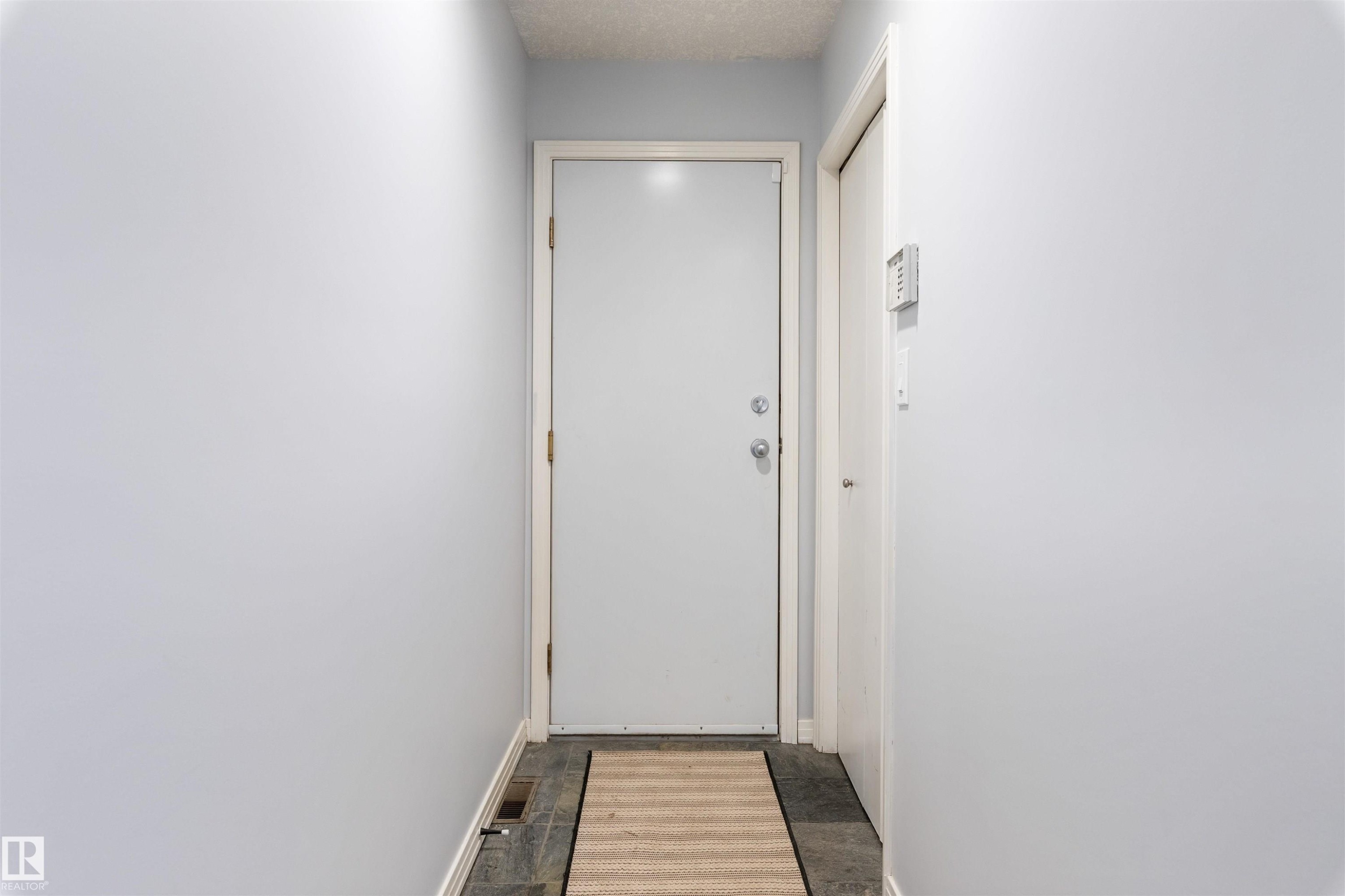 Entryway featuring a white door, light gray walls, dark tile flooring, and a textured area rug - 10 Everest Crescent, St. Albert, AB