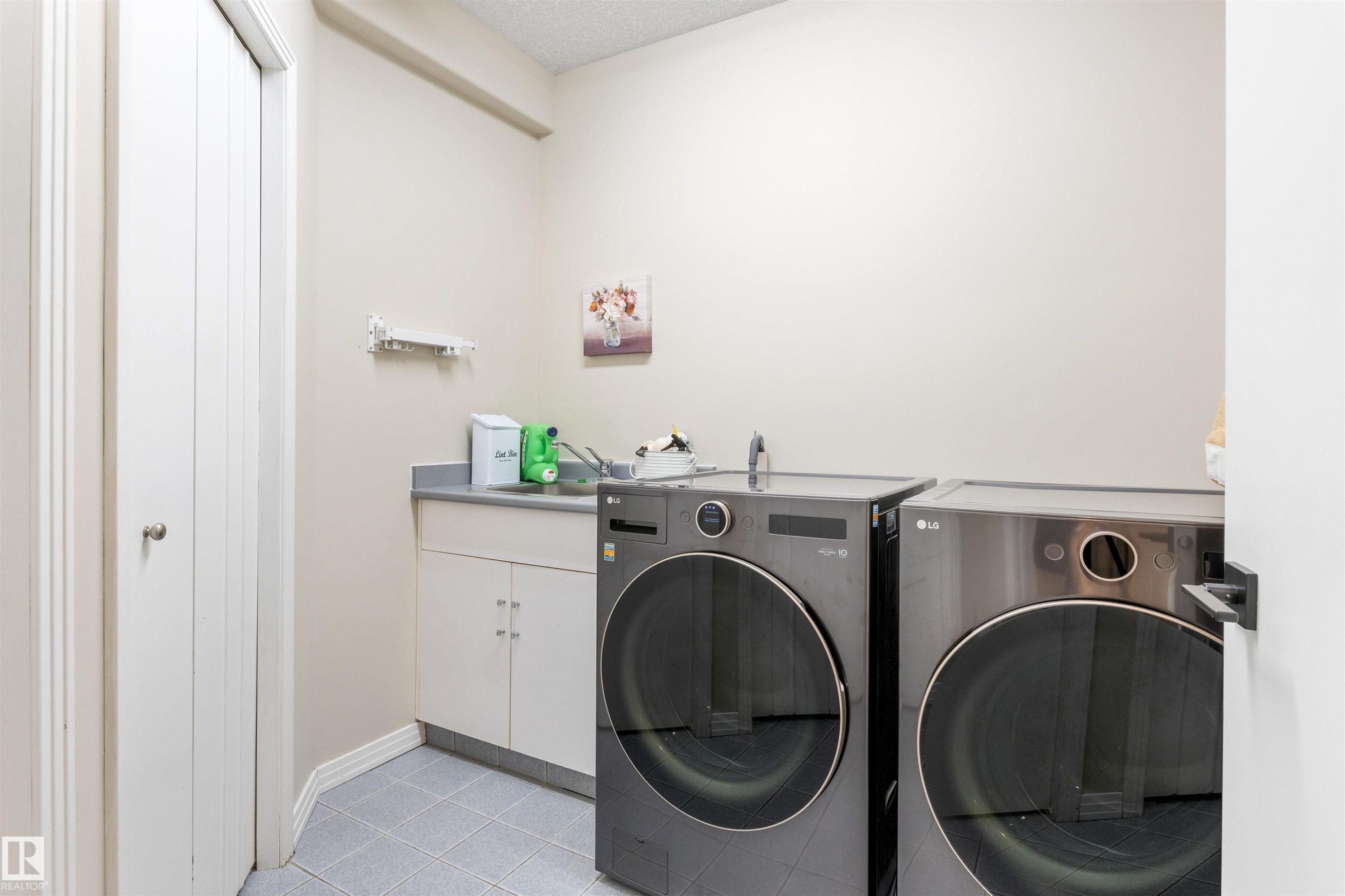 Dedicated laundry area featuring a utility sink, cabinet storage, and tile flooring - 10 Everest Crescent, St. Albert, AB