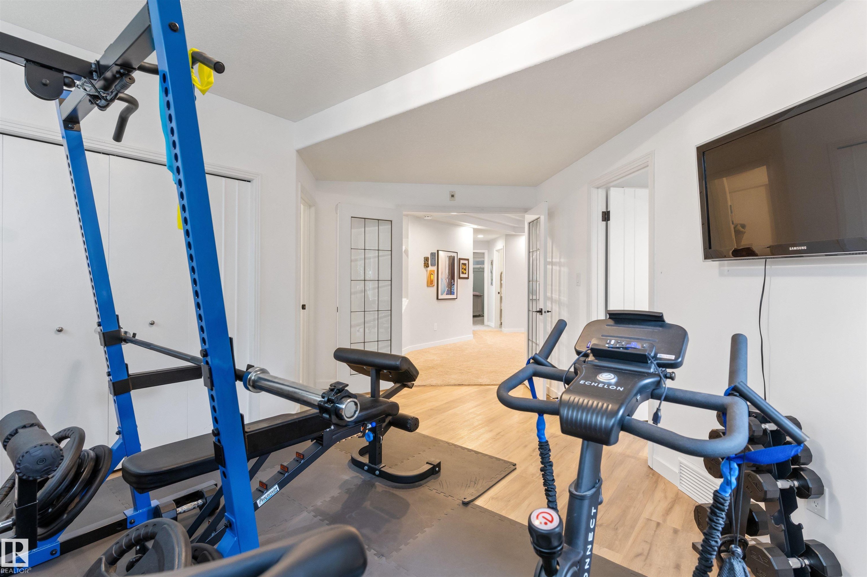 Dedicated exercise area featuring wood-finish flooring, white walls, and a wall-mounted television - 10 Everest Crescent, St. Albert, AB