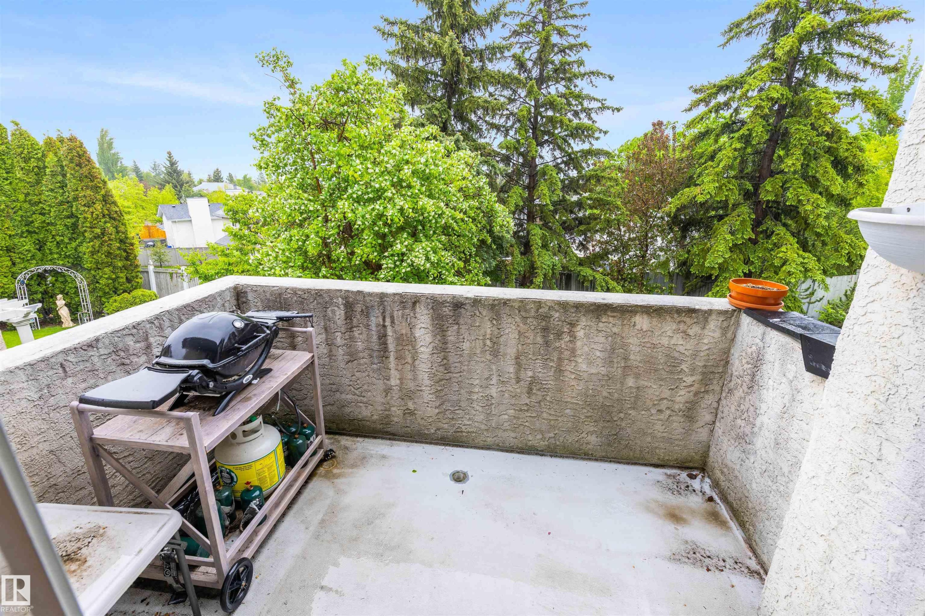 Balcony with textured concrete walls and a light-colored floor, surrounded by mature trees - 10 Everest Crescent, St. Albert, AB