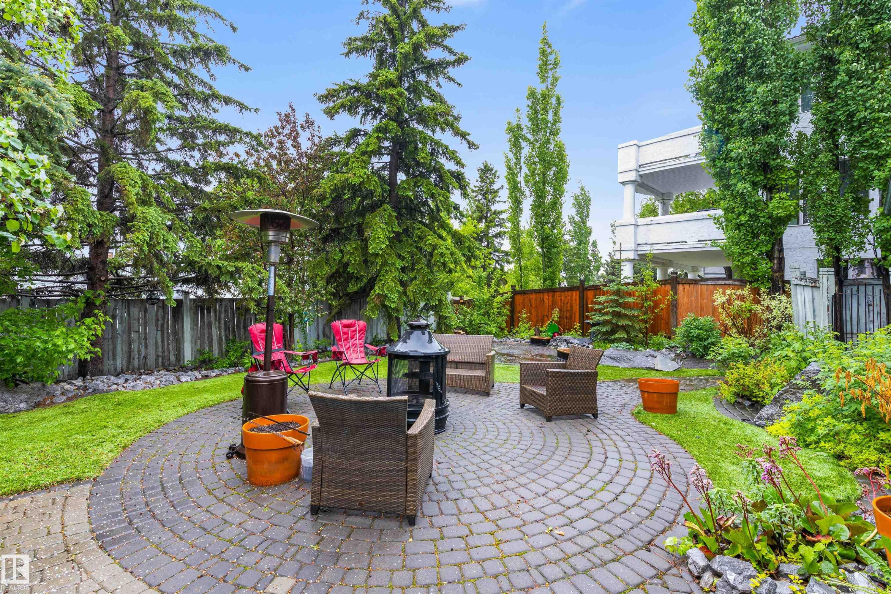 Circular paver patio with a stone fire pit, surrounded by lush landscaping and mature trees - 10 Everest Crescent, St. Albert, AB