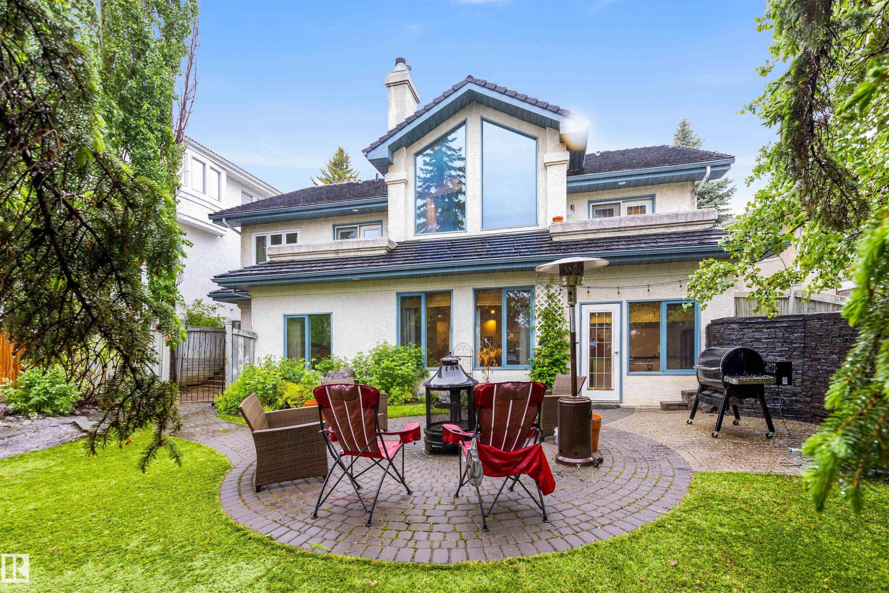 Spacious backyard featuring a circular paver patio, lush green lawn, and mature perimeter trees - 10 Everest Crescent, St. Albert, AB