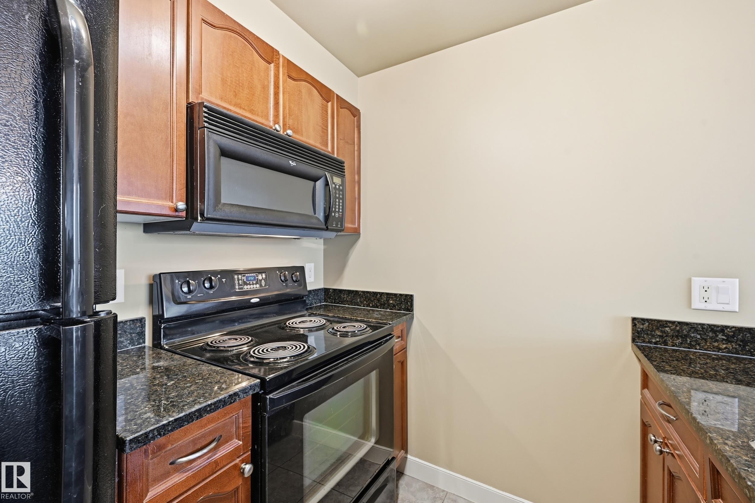 Kitchen featuring black appliances, granite countertops, wood-finish cabinetry, and an over-range microwave - #1407 9939 109 St Nw, Edmonton, AB