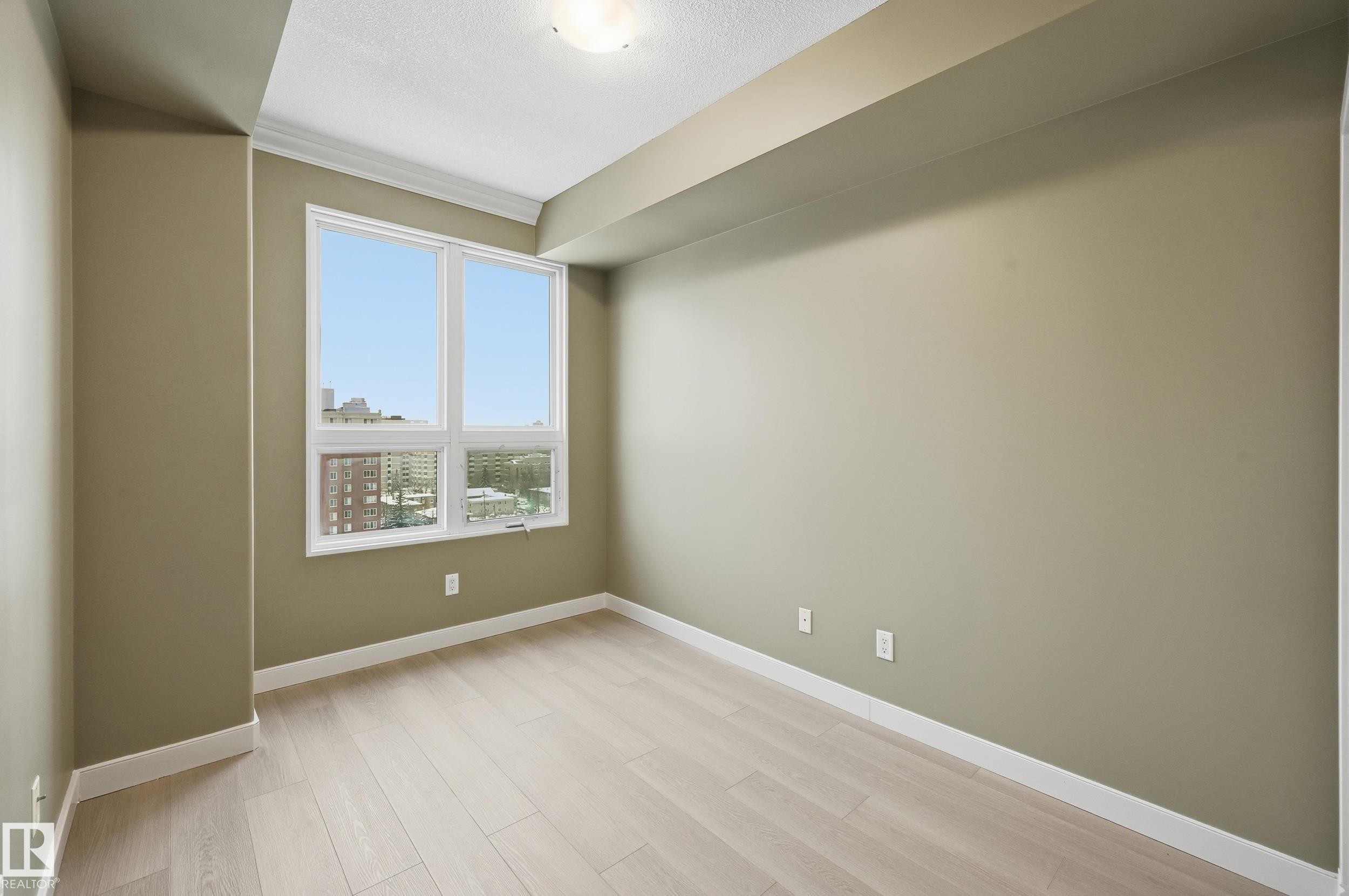 Bright interior room featuring a large window, light wood-finish flooring, and crown molding - #1407 9939 109 St Nw, Edmonton, AB
