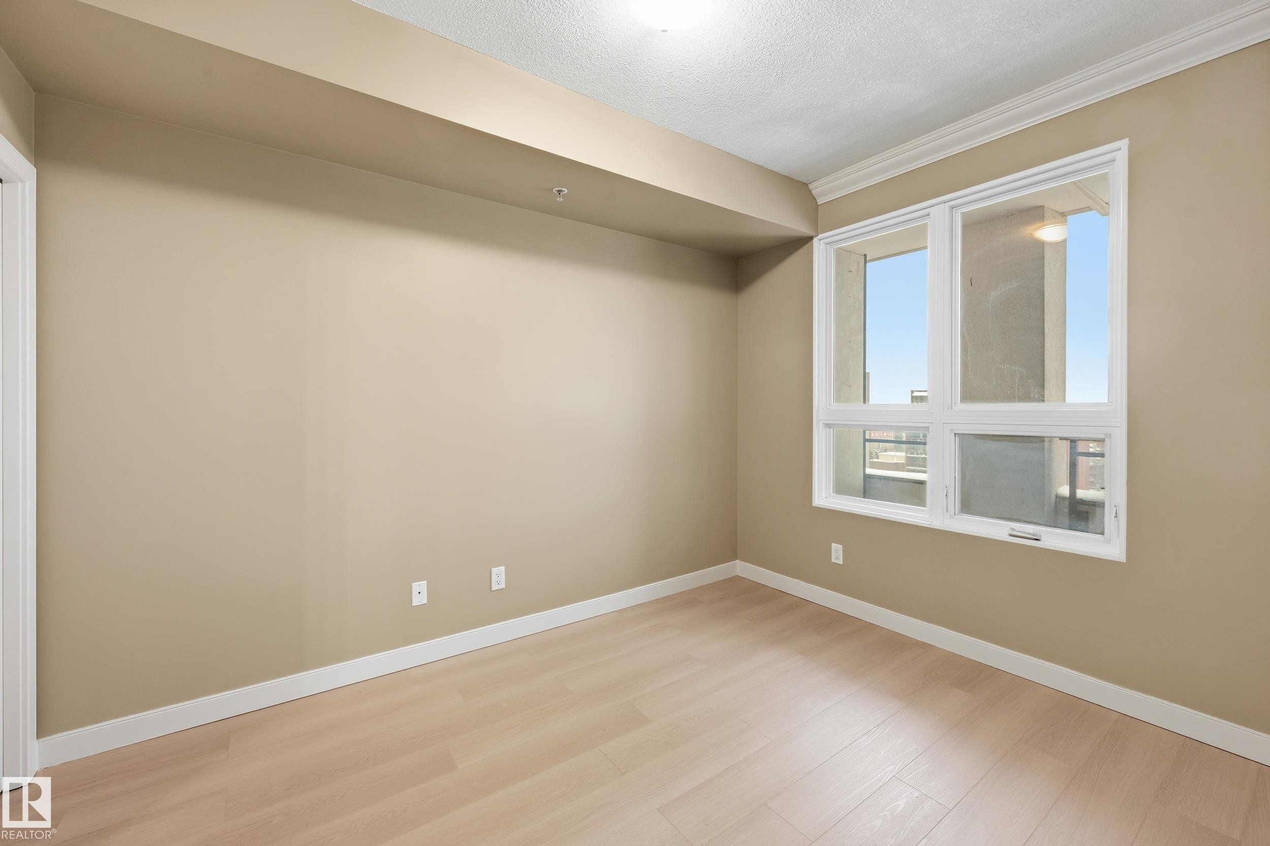 Bright room featuring a large window, crown molding, light wood-finish flooring, neutral wall tones, and white baseboards - #1407 9939 109 St Nw, Edmonton, AB