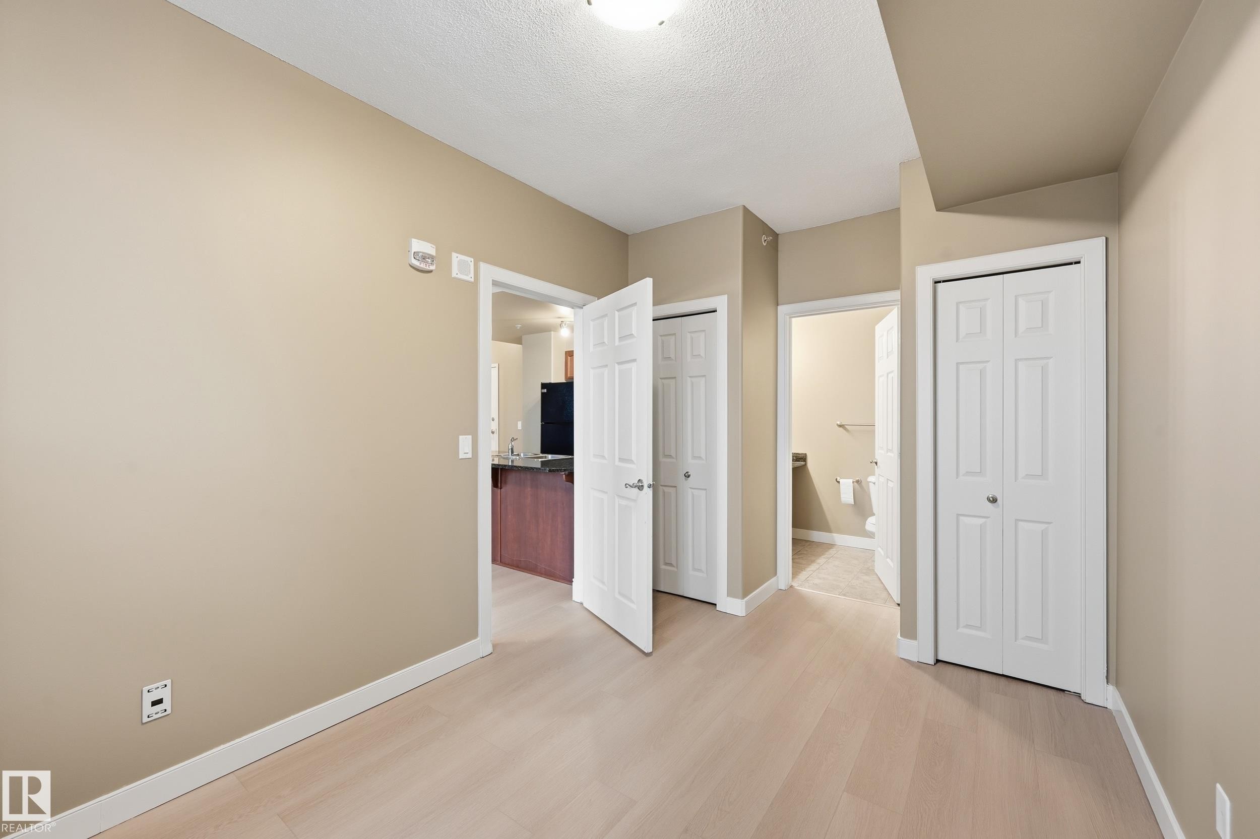 Open interior space with light wood-finish flooring, neutral wall paint, and white baseboards - #1407 9939 109 St Nw, Edmonton, AB