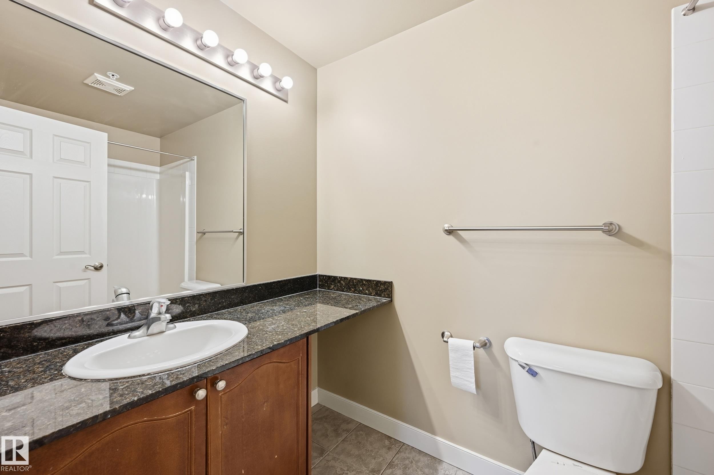 Bathroom featuring a vanity with a dark granite countertop, an undermount sink with chrome fixtures, and wood-finish cabinetry - #1407 9939 109 St Nw, Edmonton, AB