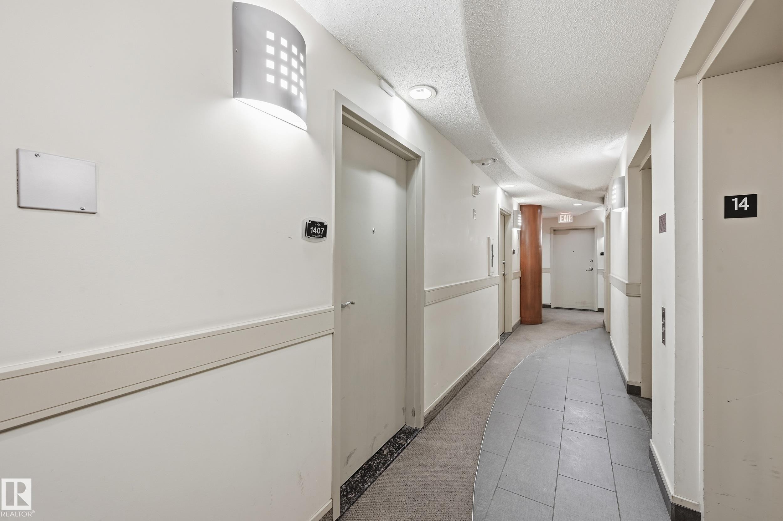 Corridor featuring contemporary wall sconce lighting, white walls, and a protective chair rail - #1407 9939 109 St Nw, Edmonton, AB