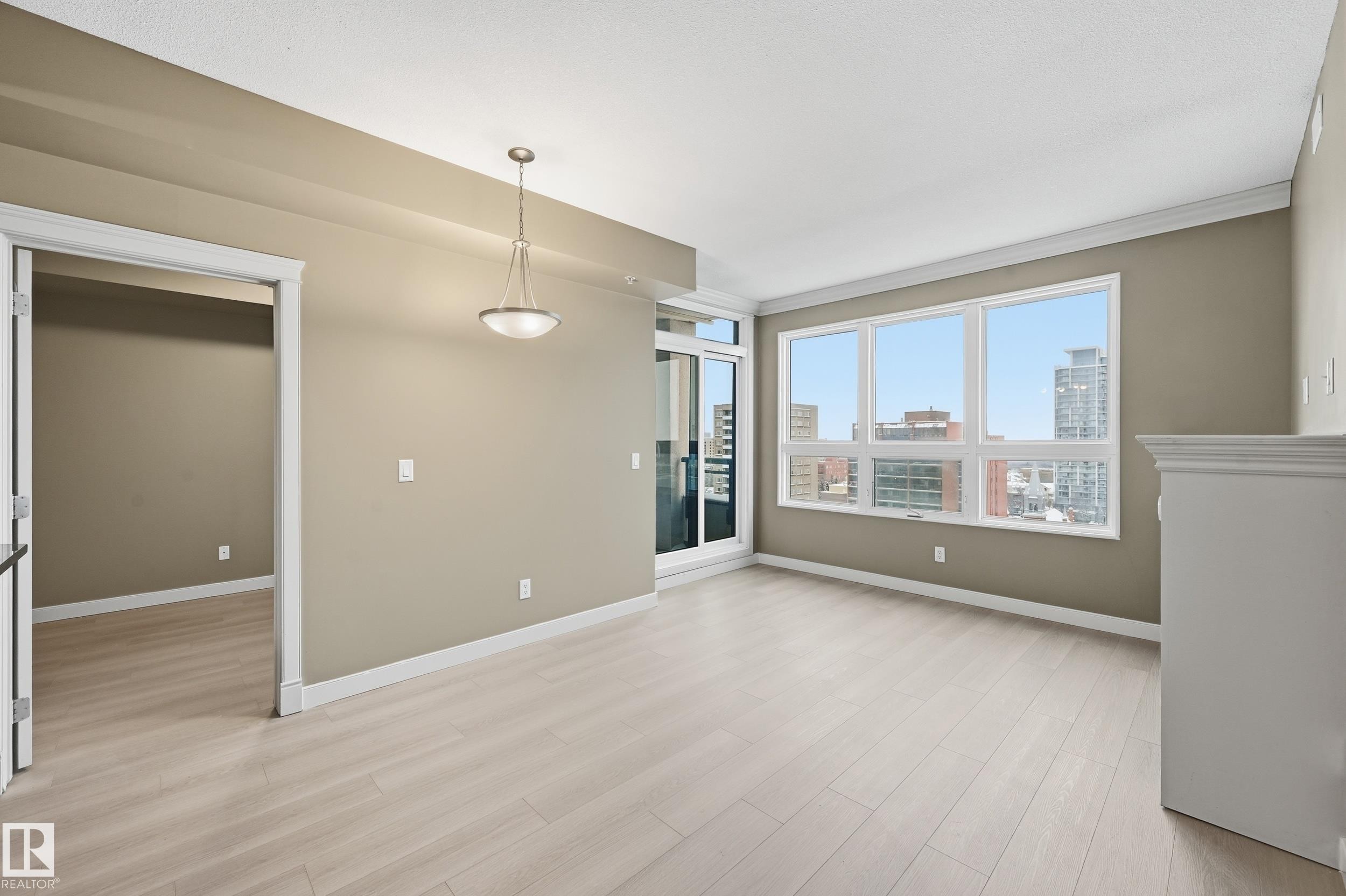 Spacious room featuring light wood-finish flooring, neutral wall tones, and a contemporary ceiling fixture - #1407 9939 109 St Nw, Edmonton, AB