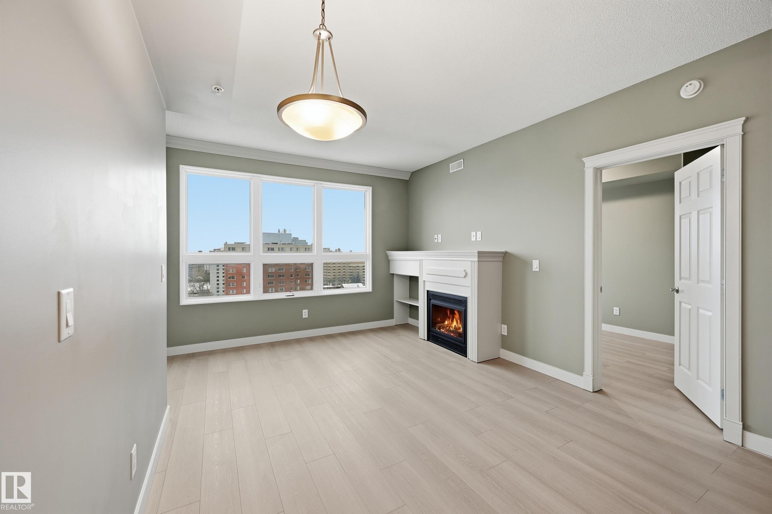 Spacious room featuring wood-finish flooring, a built-in fireplace with mantle and shelving, a multi-pane window, and an overhead decorative light fixture - #1407 9939 109 St Nw, Edmonton, AB