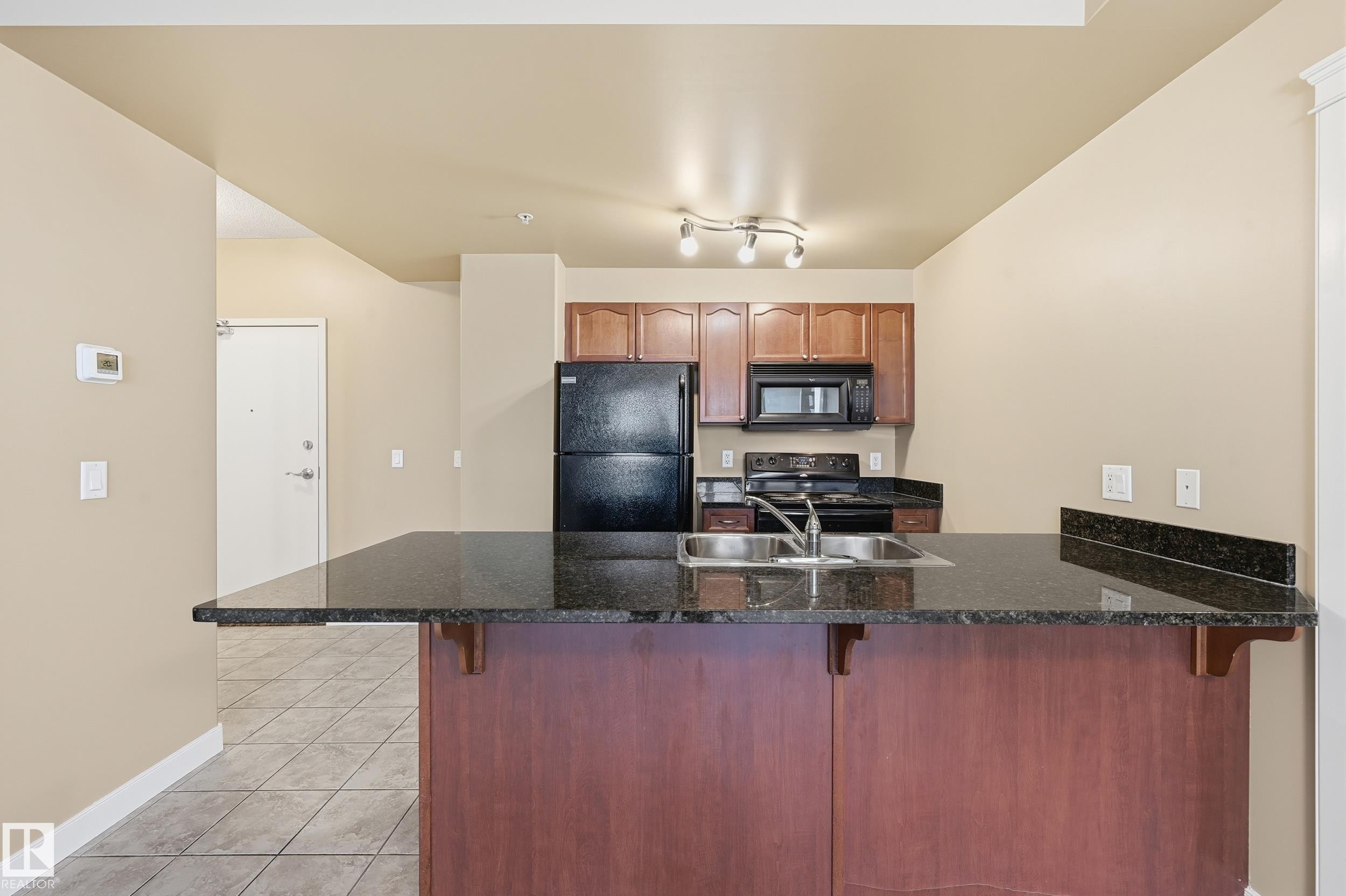 Kitchen featuring a large central island with a granite countertop, double basin sink, and rich wood-finish base - #1407 9939 109 St Nw, Edmonton, AB