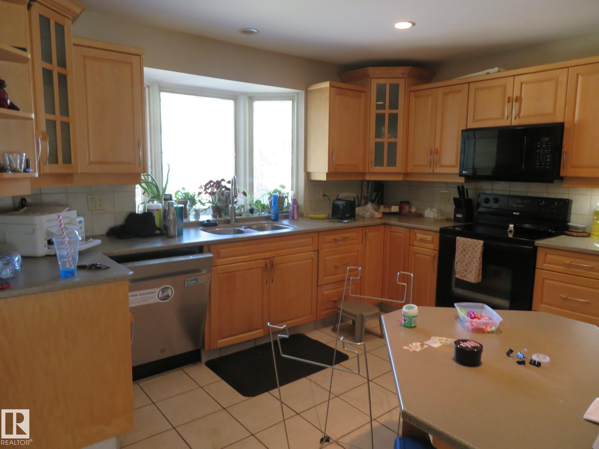 Kitchen featuring light wood cabinetry, a bay window with a double basin sink, black appliances, and neutral countertops - 10720 57 Avenue Nw, Edmonton, AB - Indoor Photo Showing Kitchen With Double Sink