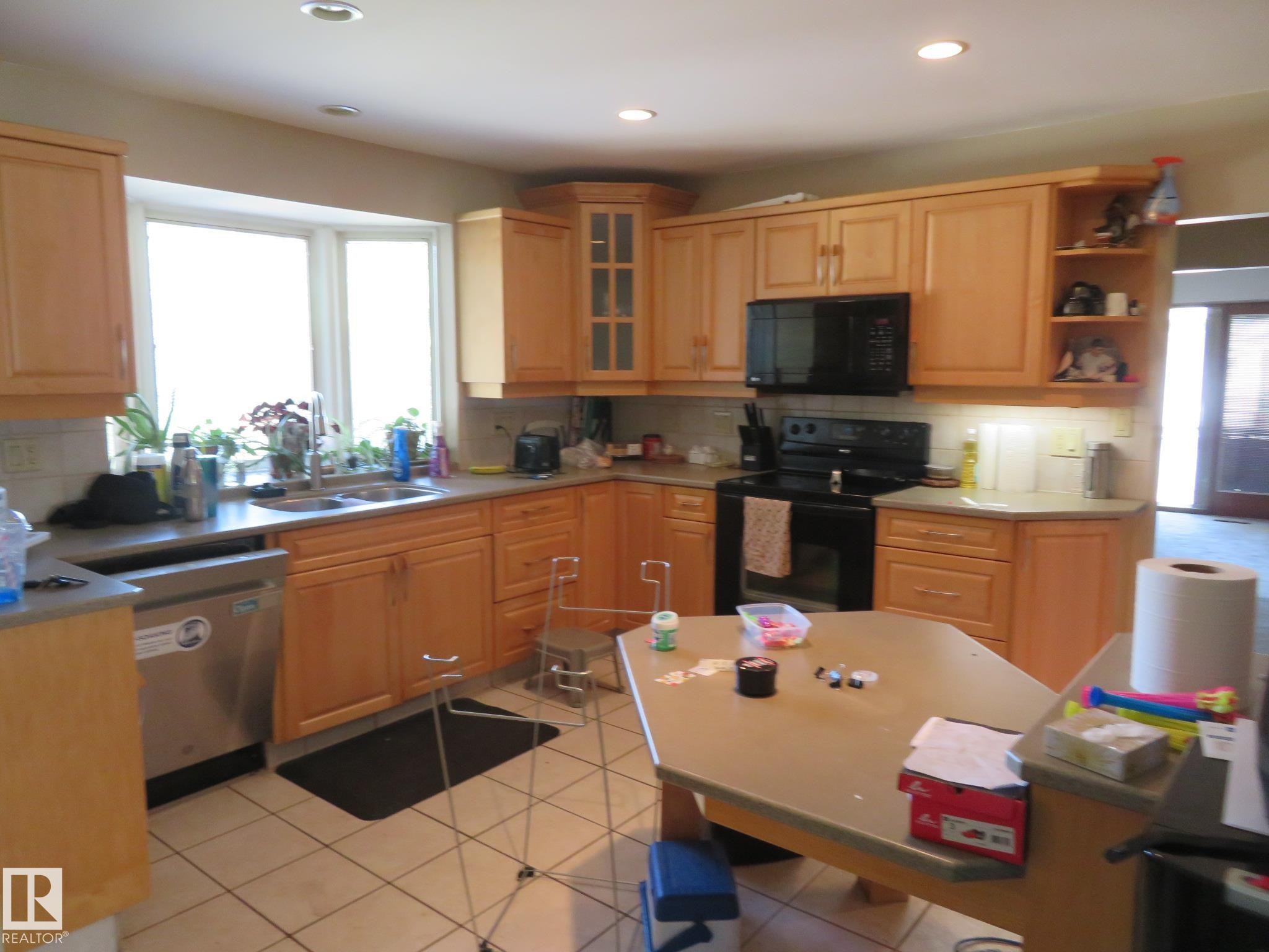 Kitchen featuring light wood cabinetry, a bay window, stainless steel dishwasher, black range, and an integrated microwave - 10720 57 Avenue Nw, Edmonton, AB - Indoor Photo Showing Kitchen With Double Sink