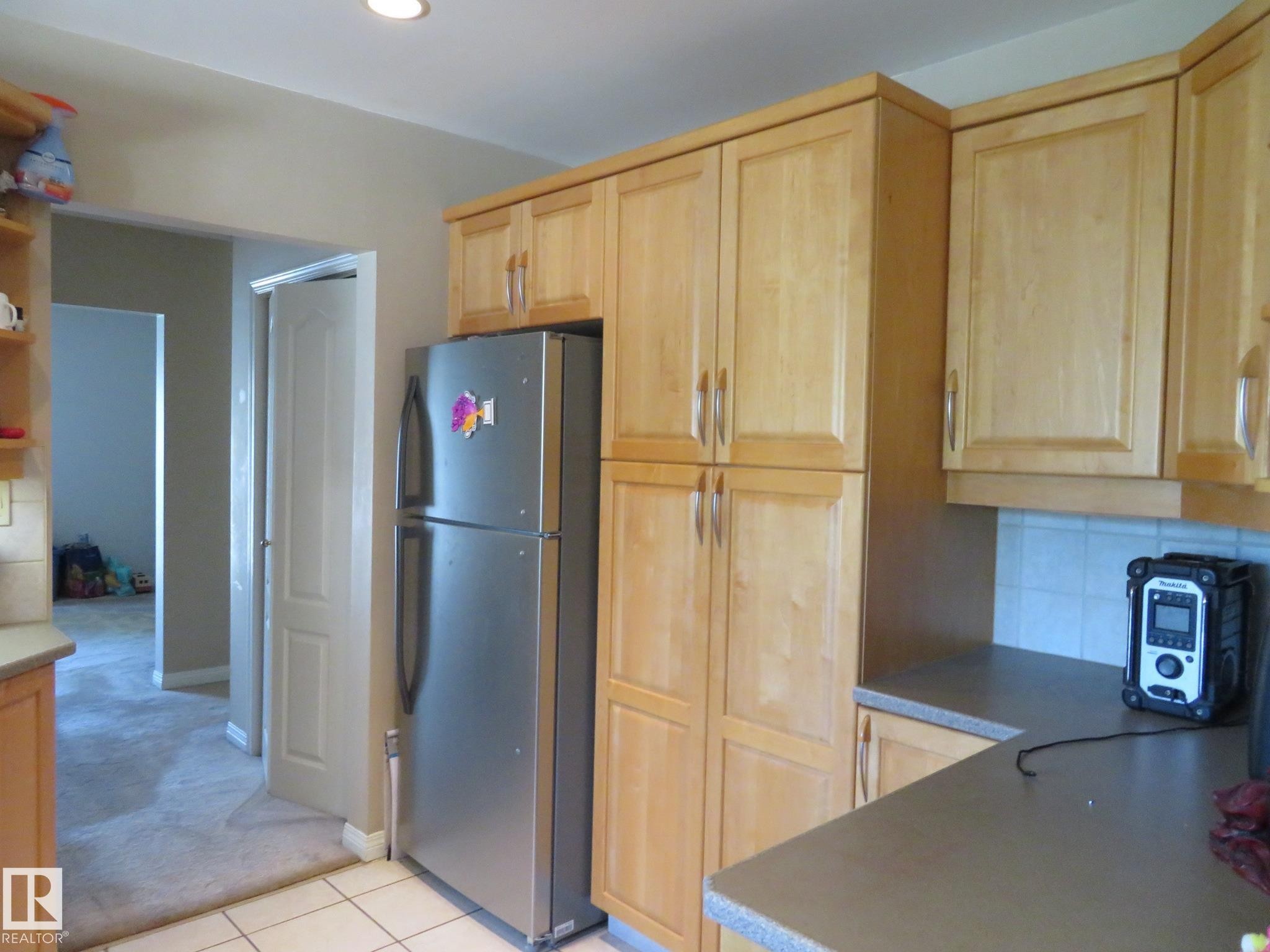 Kitchen featuring light wood cabinetry, white tile flooring, and a stainless steel refrigerator - 10720 57 Avenue Nw, Edmonton, AB - Indoor Photo Showing Kitchen