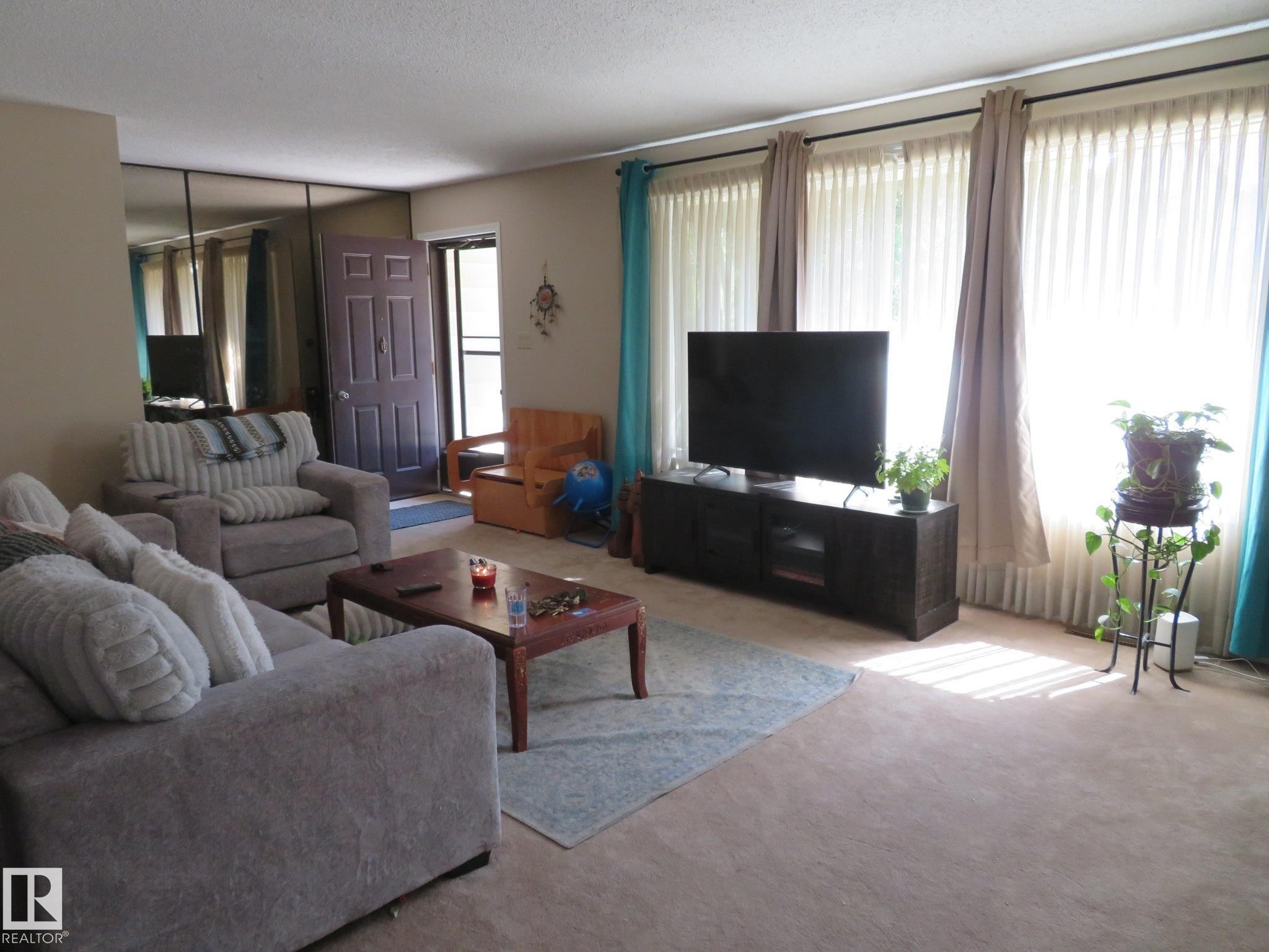 Living area with wall-to-wall carpeting and a full mirrored wall - 10720 57 Avenue Nw, Edmonton, AB - Indoor Photo Showing Living Room