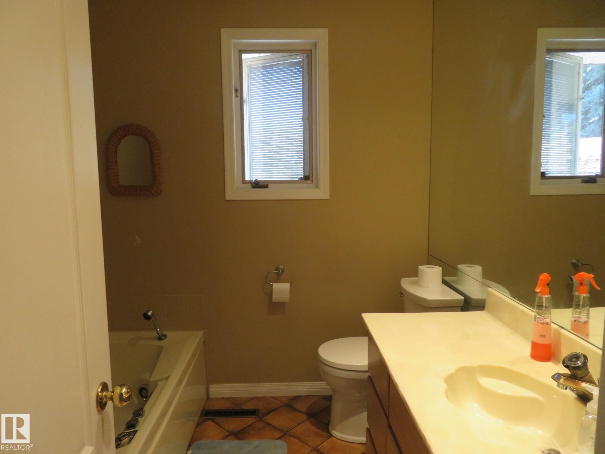 Bathroom featuring a full vanity with an integrated sink, a large wall-mounted mirror, a standard toilet, and a bathtub with a shower fixture - 10720 57 Avenue Nw, Edmonton, AB - Indoor Photo Showing Bathroom