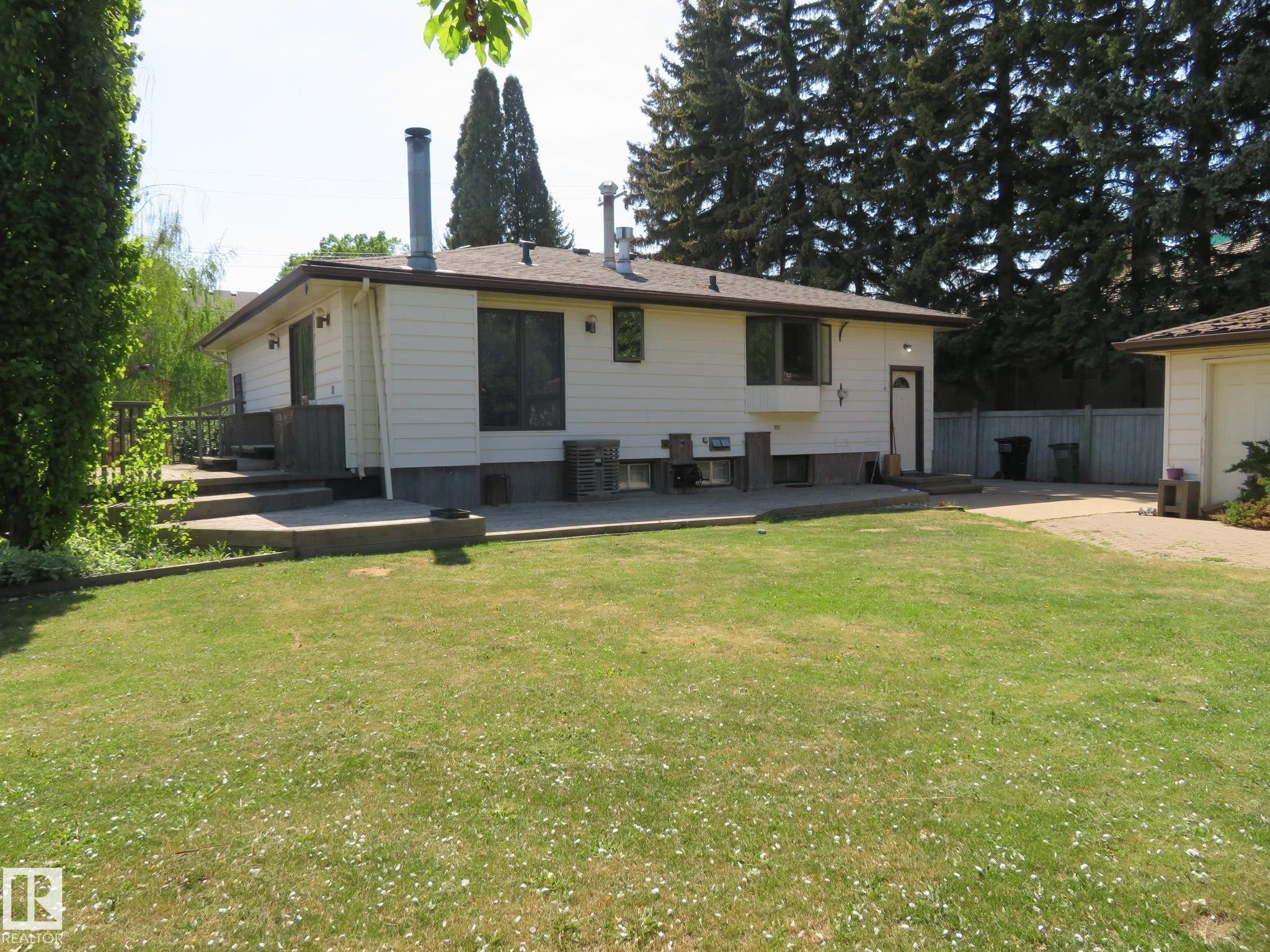 Expansive green space featuring a large lawn area, a concrete patio, and a multi-level deck - 10720 57 Avenue Nw, Edmonton, AB - Outdoor