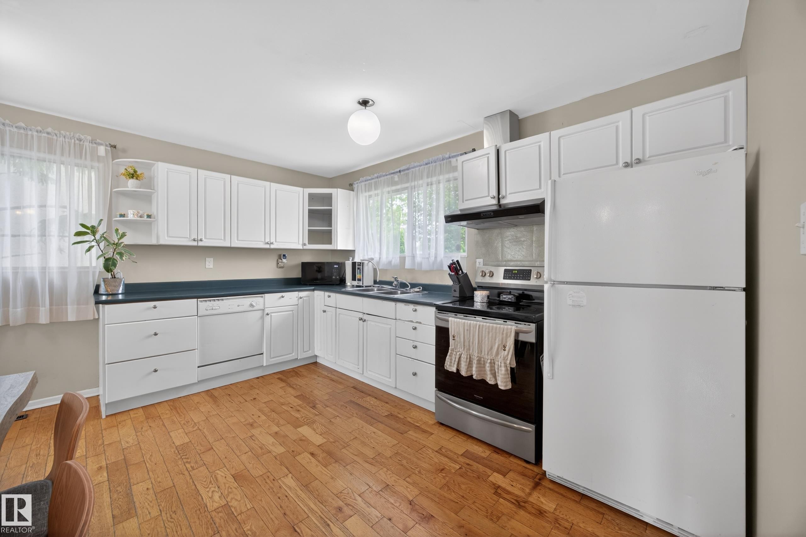Kitchen featuring wood-finish flooring, white cabinetry, dark countertops, and stainless steel appliances including a range and refrigerator - 5216 104A Street, Edmonton, AB - Indoor Photo Showing Kitchen