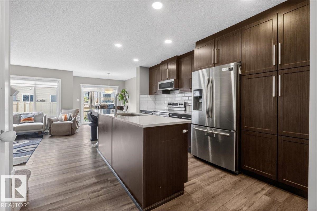 Modern kitchen featuring dark wood-finish cabinetry, stainless steel appliances, and a central island with a light-toned countertop - 223 40A Avenue, Edmonton, AB - Indoor Photo Showing Kitchen