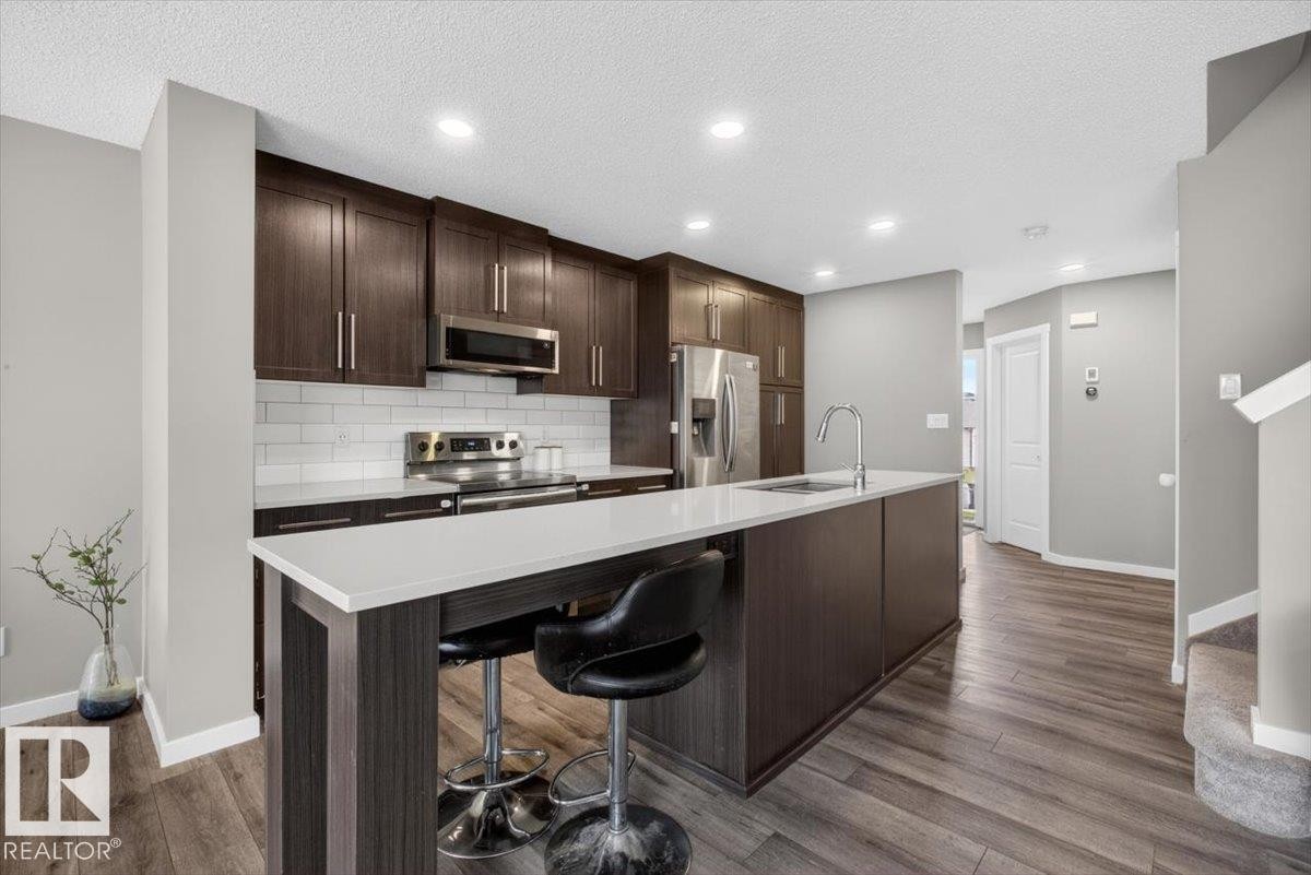 Modern kitchen featuring dark wood-finish cabinetry, white subway tile backsplash, stainless steel appliances, and an expansive island with a white countertop - 223 40A Avenue, Edmonton, AB - Indoor Photo Showing Kitchen With Upgraded Kitchen