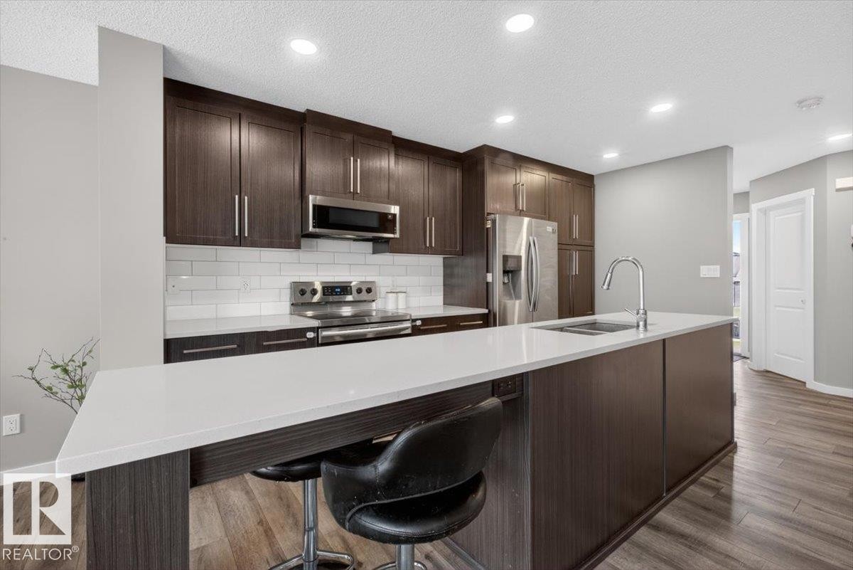Modern kitchen featuring a large center island with integrated sink, stainless steel appliances, dark wood-finish cabinetry, white subway tile backsplash, and recessed lighting - 223 40A Avenue, Edmonton, AB - Indoor Photo Showing Kitchen With Upgraded Kitchen