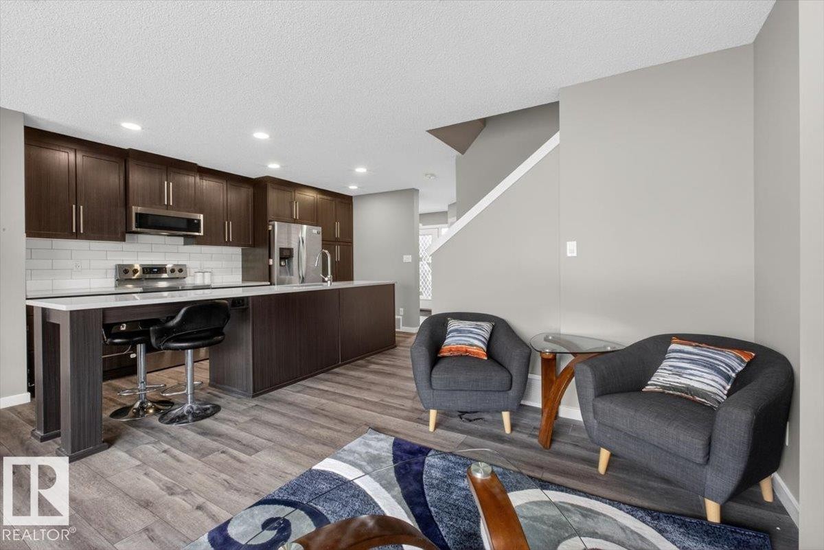 Open-concept kitchen featuring dark wood-finish cabinetry, stainless steel appliances, and a white subway tile backsplash - 223 40A Avenue, Edmonton, AB - Indoor Photo Showing Other Room