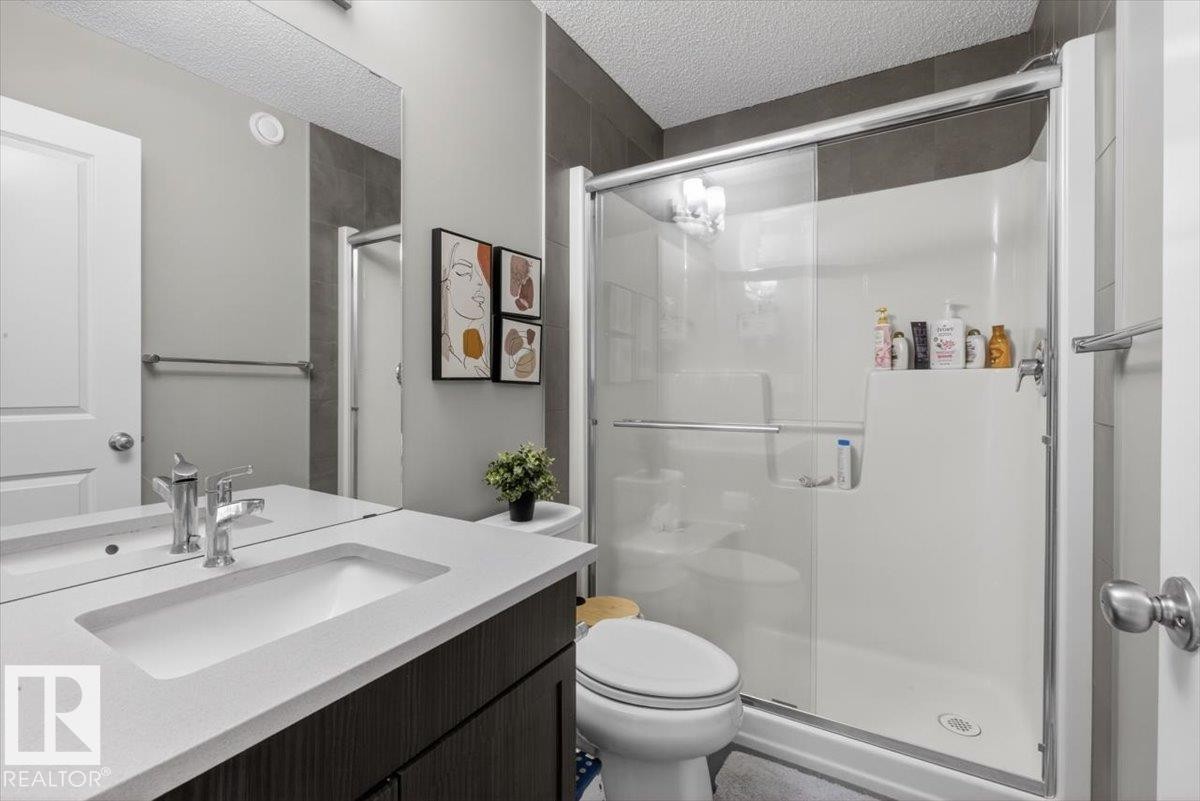 Bathroom featuring a dark wood-finish vanity with a light countertop, an integrated rectangular sink, a polished chrome faucet, a spacious mirror, and a glass-enclosed shower with a white surround - 223 40A Avenue, Edmonton, AB - Indoor Photo Showing Bathroom